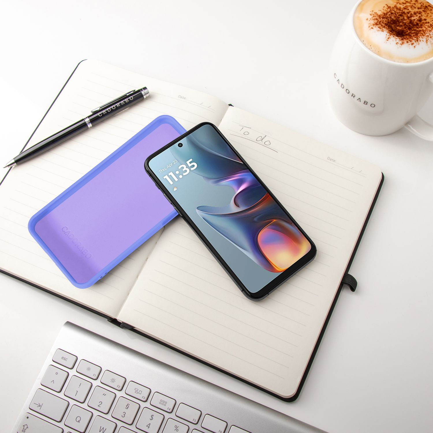 Ein Smartphone, Notizbuch, Stift, Tastatur und Kaffee liegen auf einem Schreibtisch.