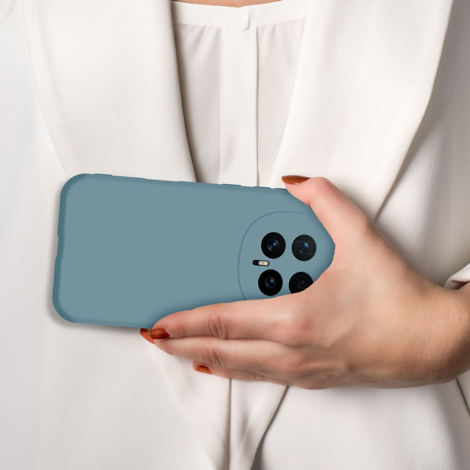 Eine Hand hält ein blaues Smartphone mit vier Kameras vor einem weißen Hemd.