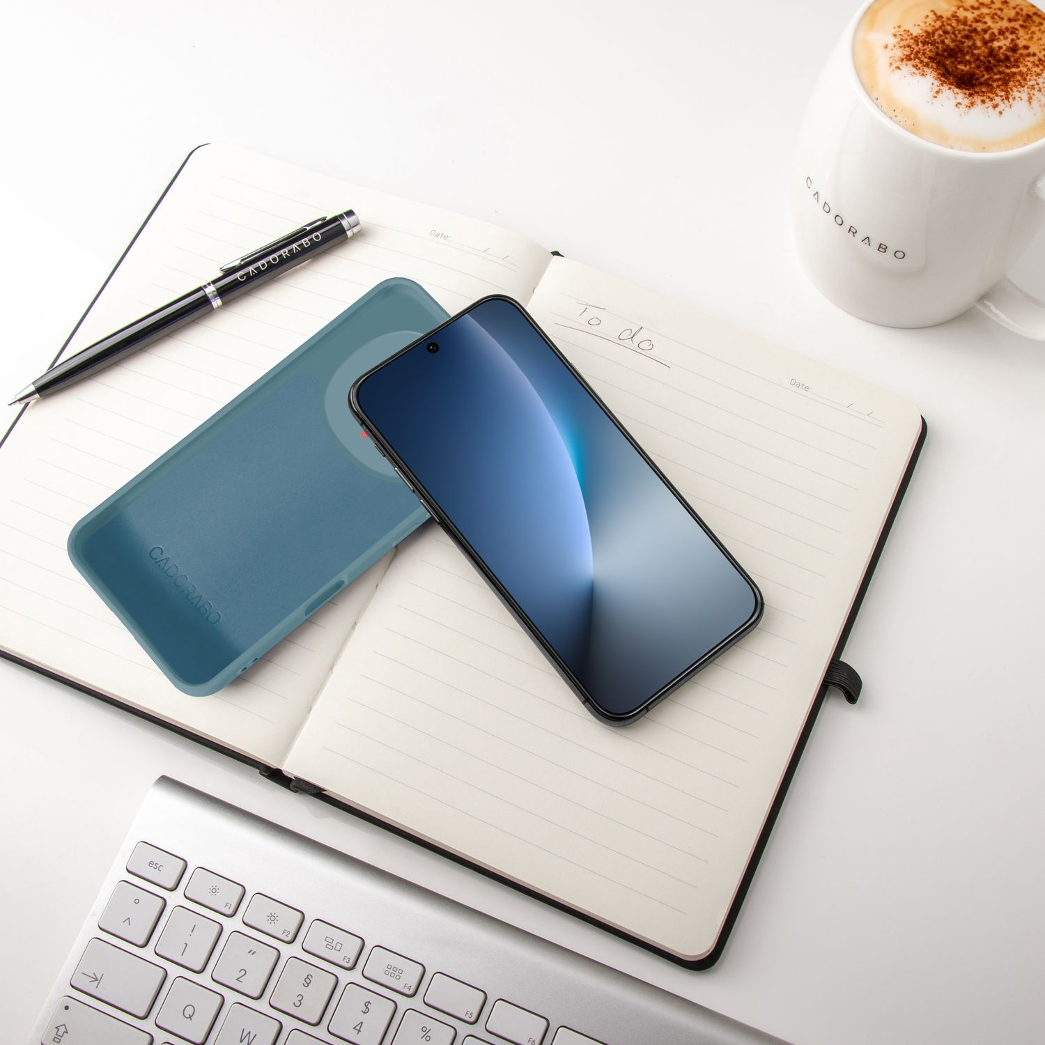 Ein aufgeschlagenes Notizbuch mit einem Smartphone, Stift, Hülle und Kaffee.