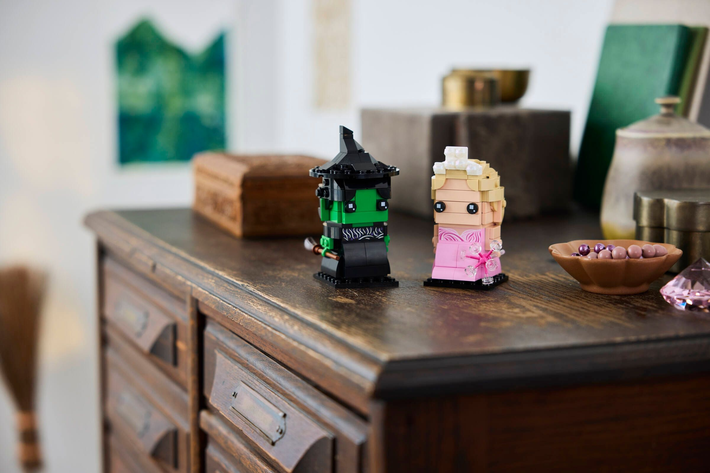 Zwei Lego-Figuren, eine grüne Hexe und eine blonde Prinzessin, stehen auf einer Kommode.