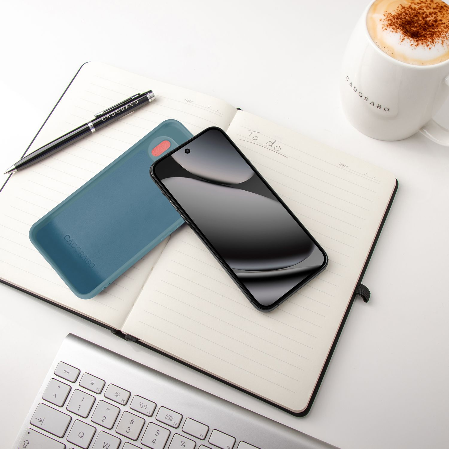 Ein schwarzes Smartphone liegt auf einem Notizbuch neben einer blauen Handyhülle.