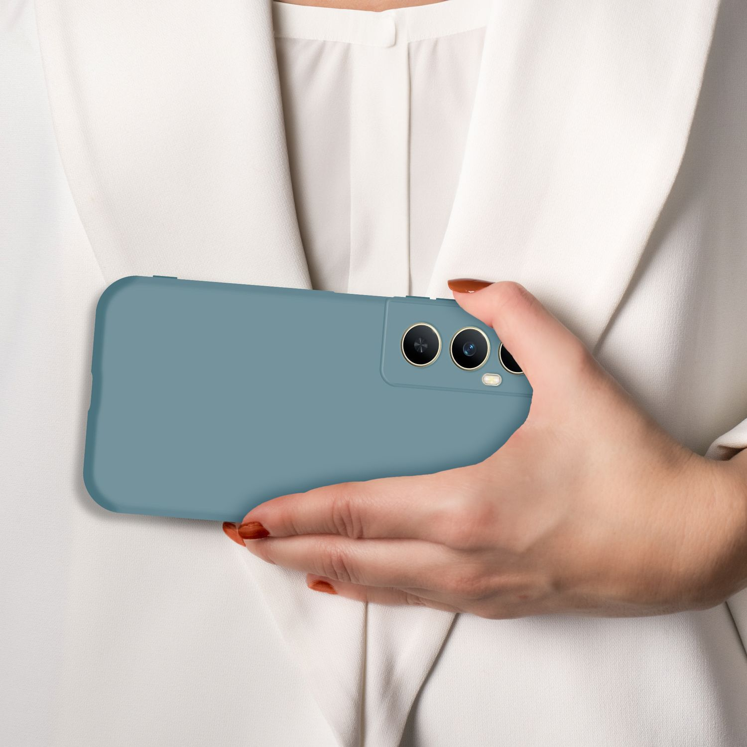 Eine Hand hält ein blaues Handy mit drei Kameras vor einem weißen Hemd.