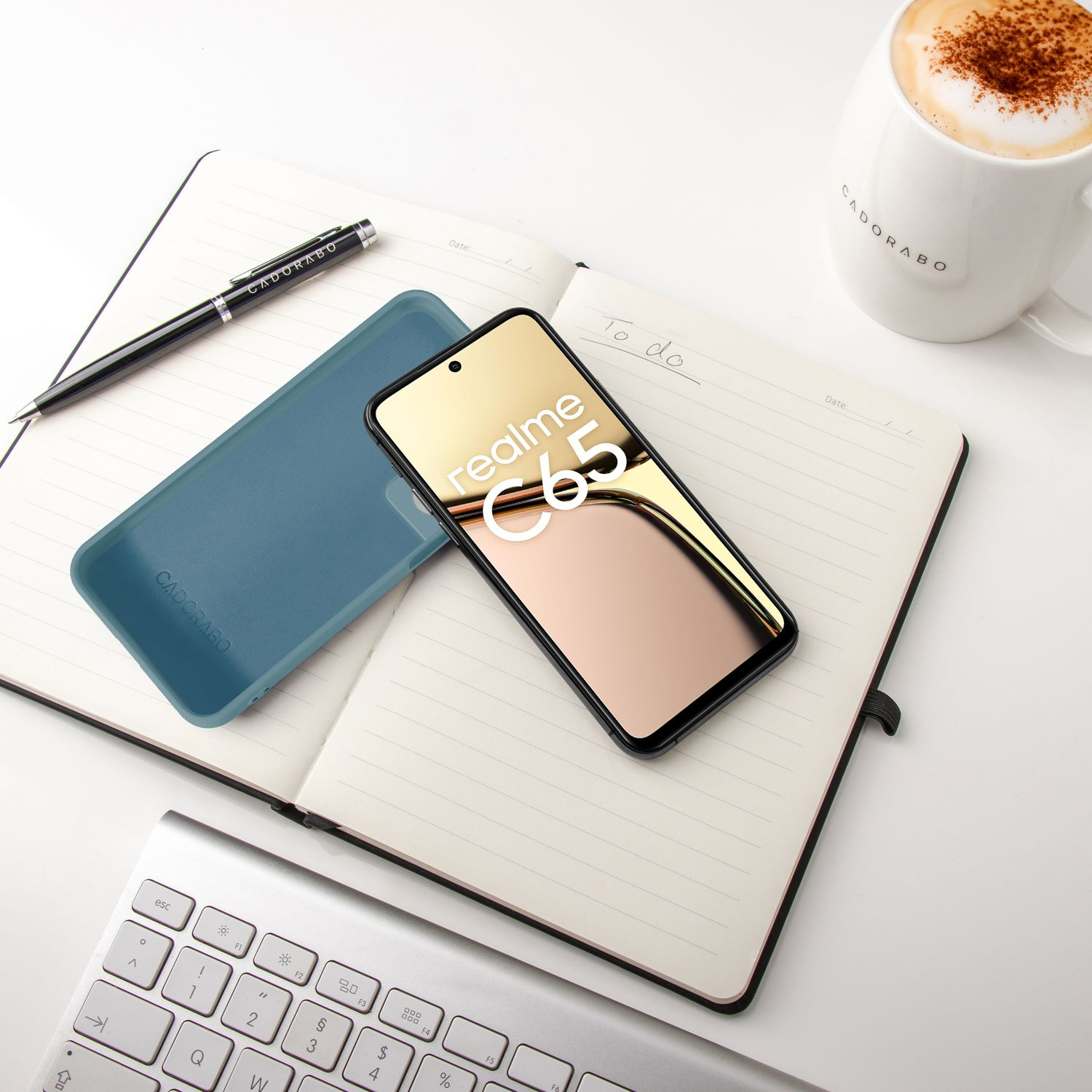 Ein Smartphone mit "realme C65" liegt auf einem Notizbuch neben einer Kaffeetasse.