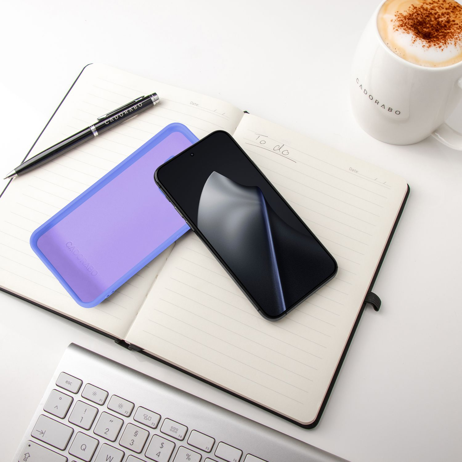 Ein offenes Notizbuch mit einem Smartphone, einer lila Hülle, einem Stift und einer Kaffeetasse.