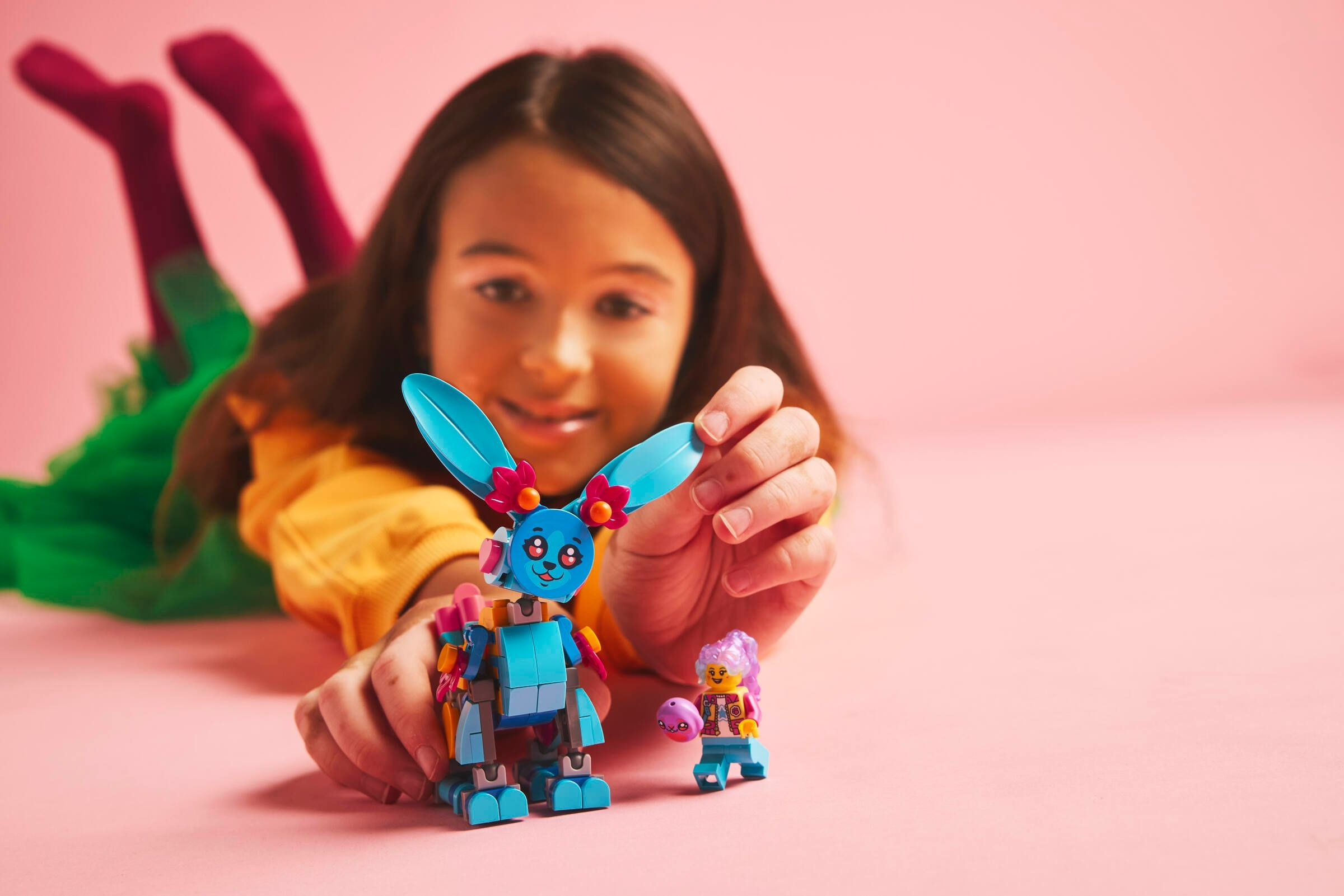Ein Mädchen baut einen blauen Lego-Hasen mit einer Minifigur auf rosa Untergrund.