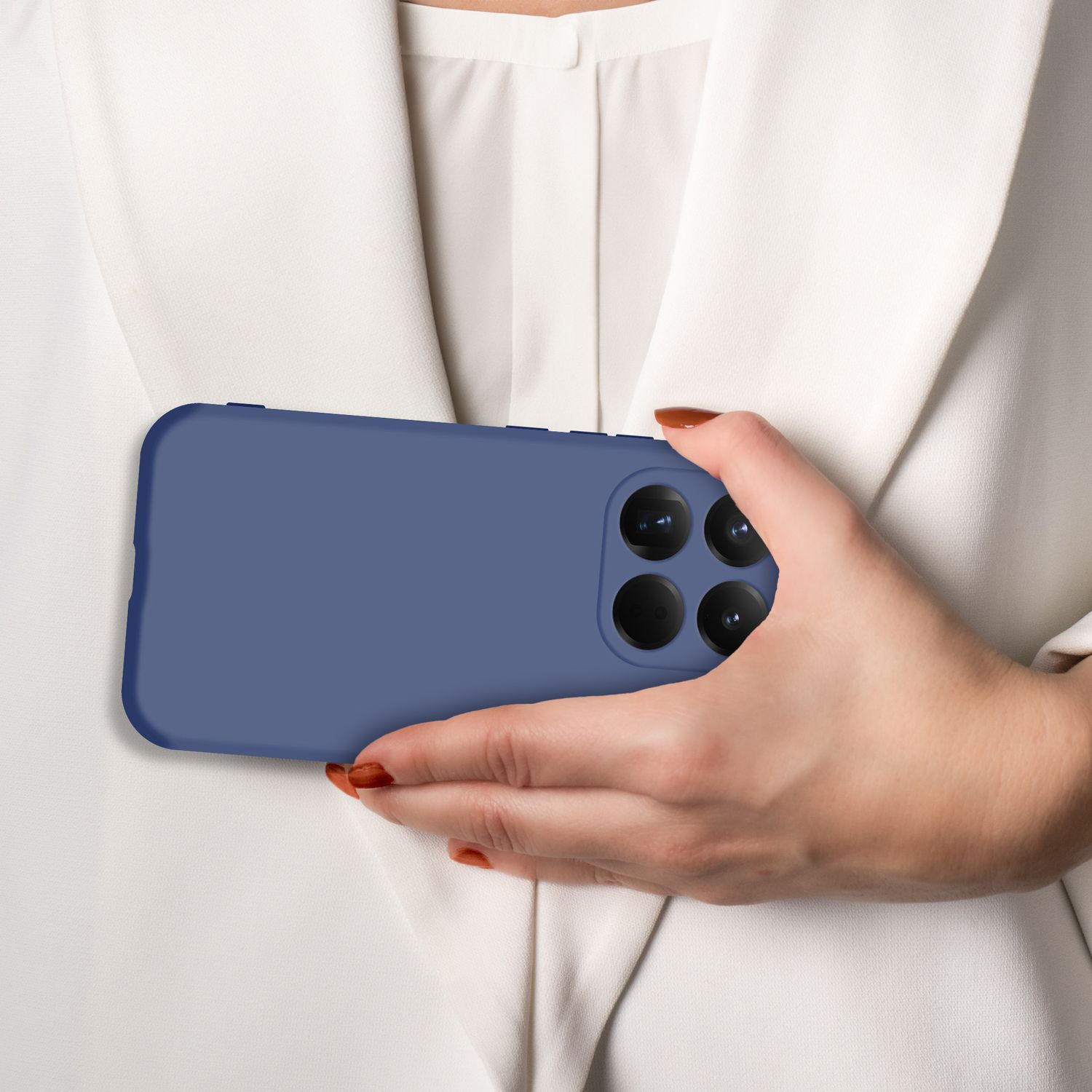 Eine Hand hält ein blaues Smartphone mit vier Kameras vor einem weißen Blazer.