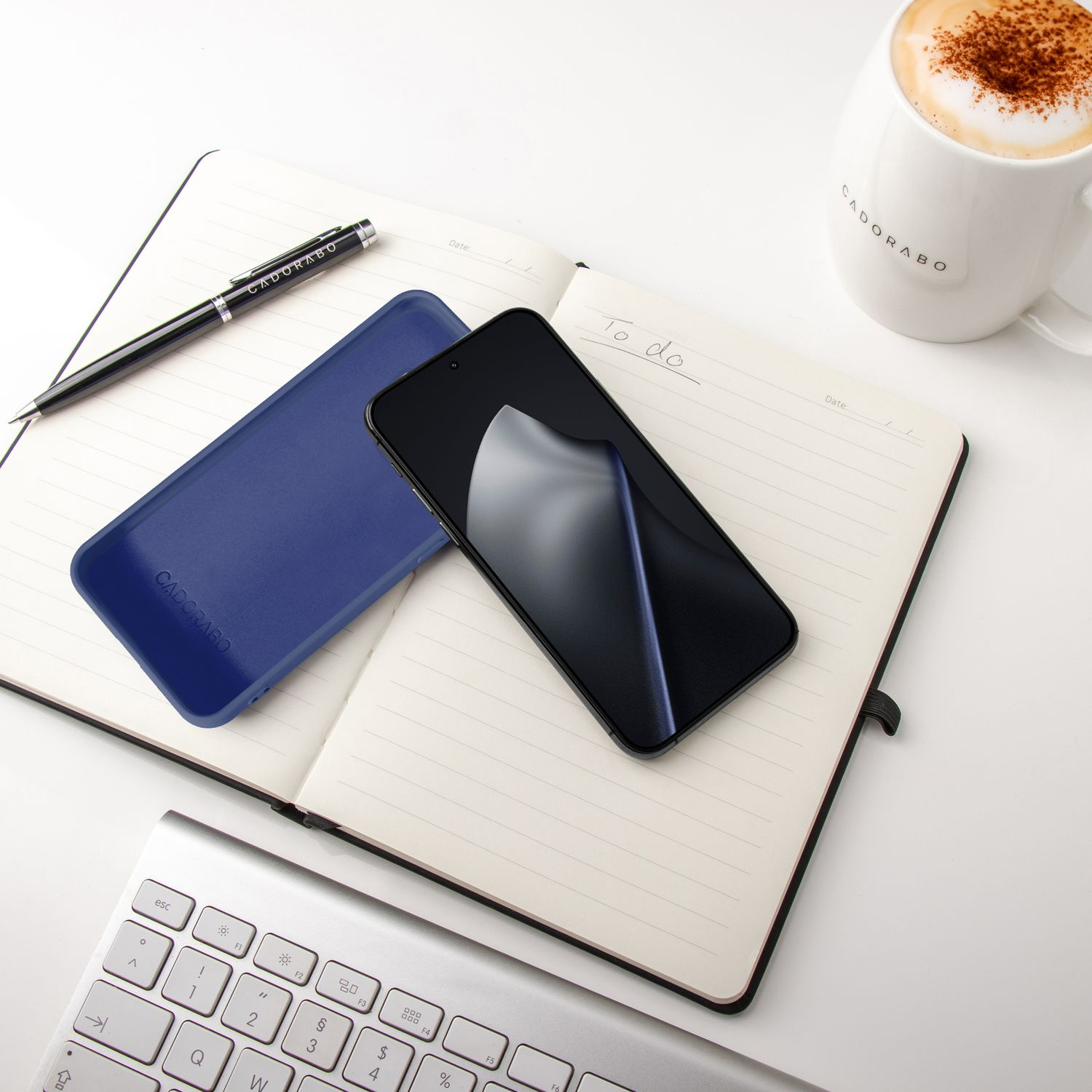 Ein offenes Notizbuch mit Stift, Handy, Hülle und Kaffee auf einem Schreibtisch.
