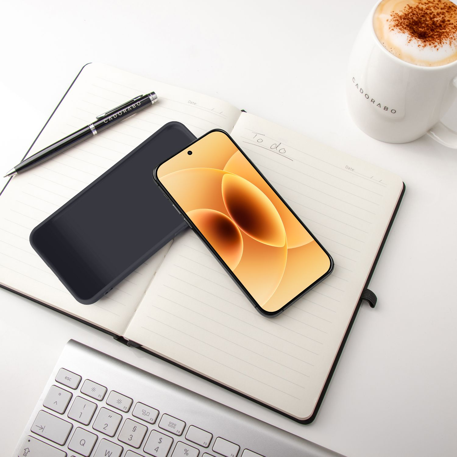 Ein Smartphone, Notizbuch, Stift und Tastatur liegen auf einem Tisch.