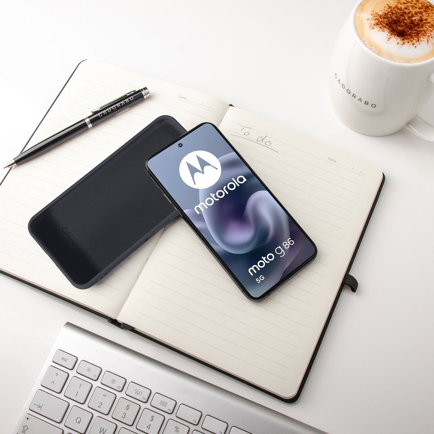 Motorola Handy, Notizbuch, Stift, Tasse Kaffee und Tastatur auf weißem Tisch.