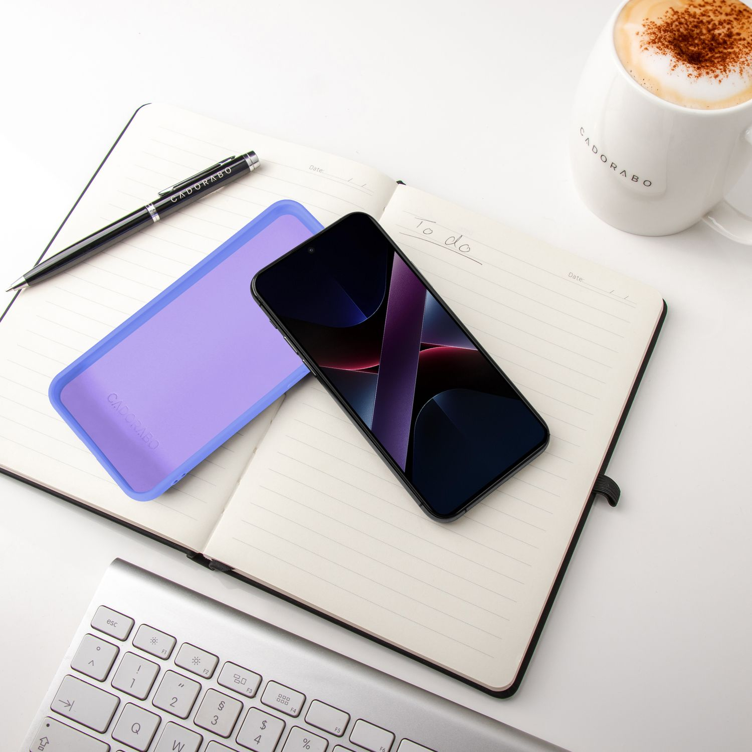 Ein aufgeschlagenes Notizbuch mit Handy, Stift, Tastatur und Kaffee.