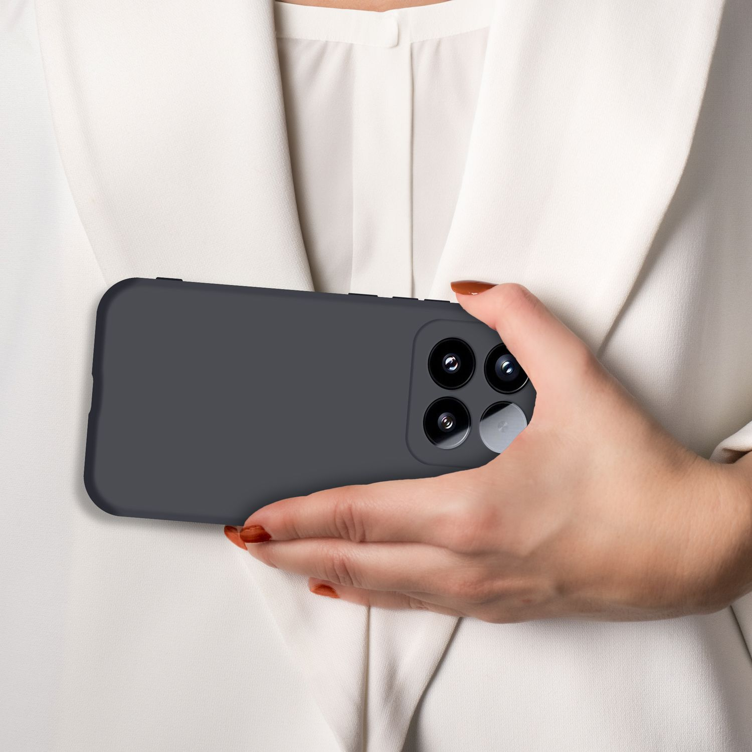 Eine Hand hält ein dunkles Smartphone mit vier Kameras vor einem weißen Hemd.