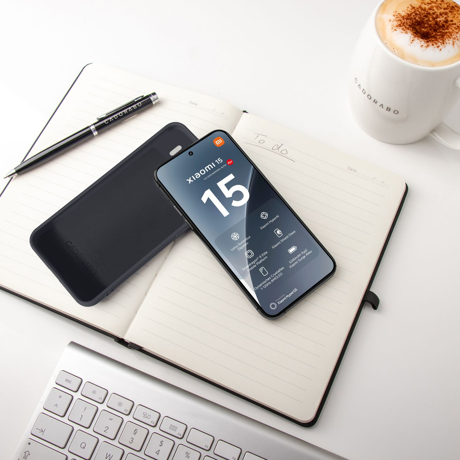 Ein Smartphone liegt auf einem Notizbuch neben einer Kaffeetasse und Tastatur.