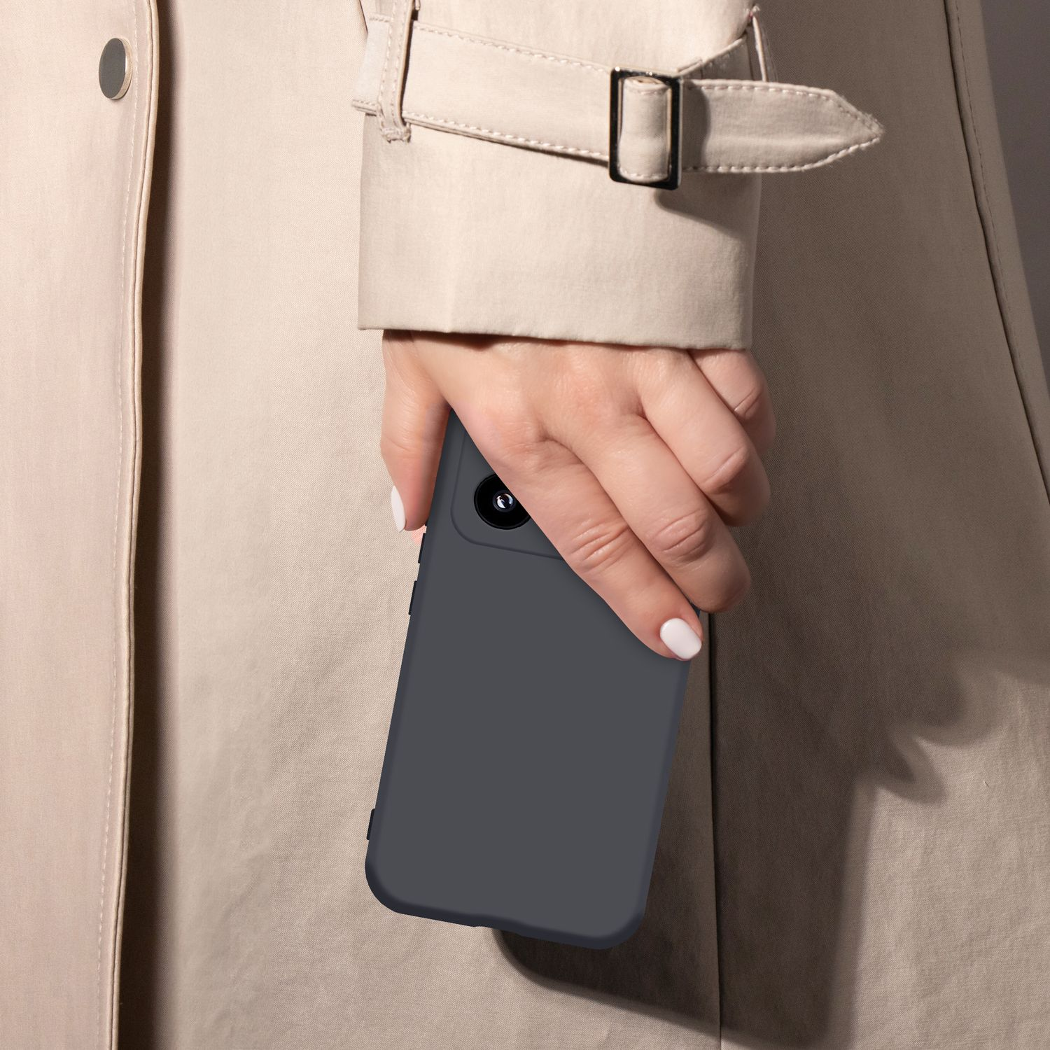 Eine Hand mit weißen Nägeln hält ein dunkles Smartphone vor einem beigen Trenchcoat.