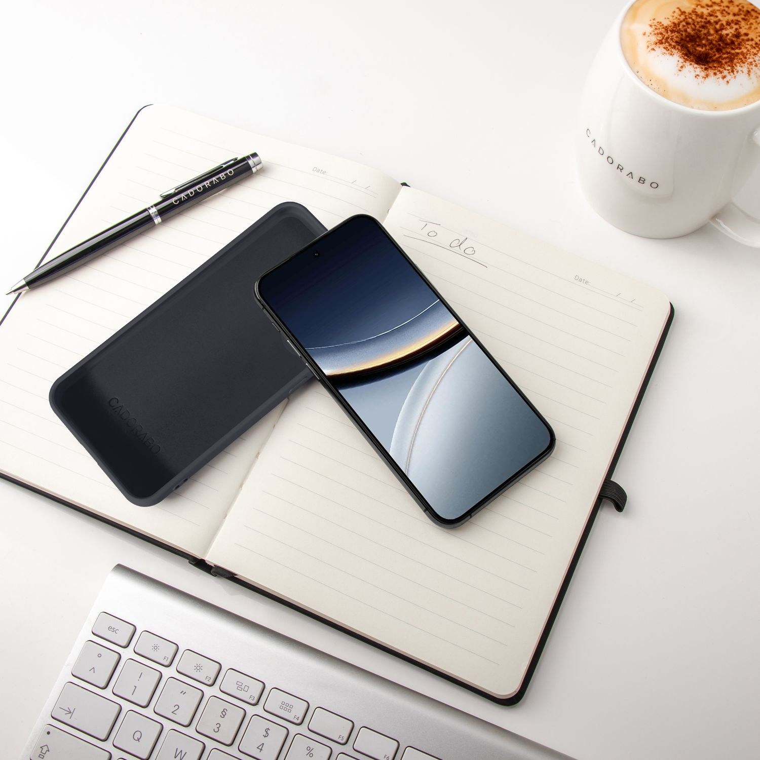 Ein Smartphone liegt auf einem Notizbuch neben einer Tasse Kaffee.