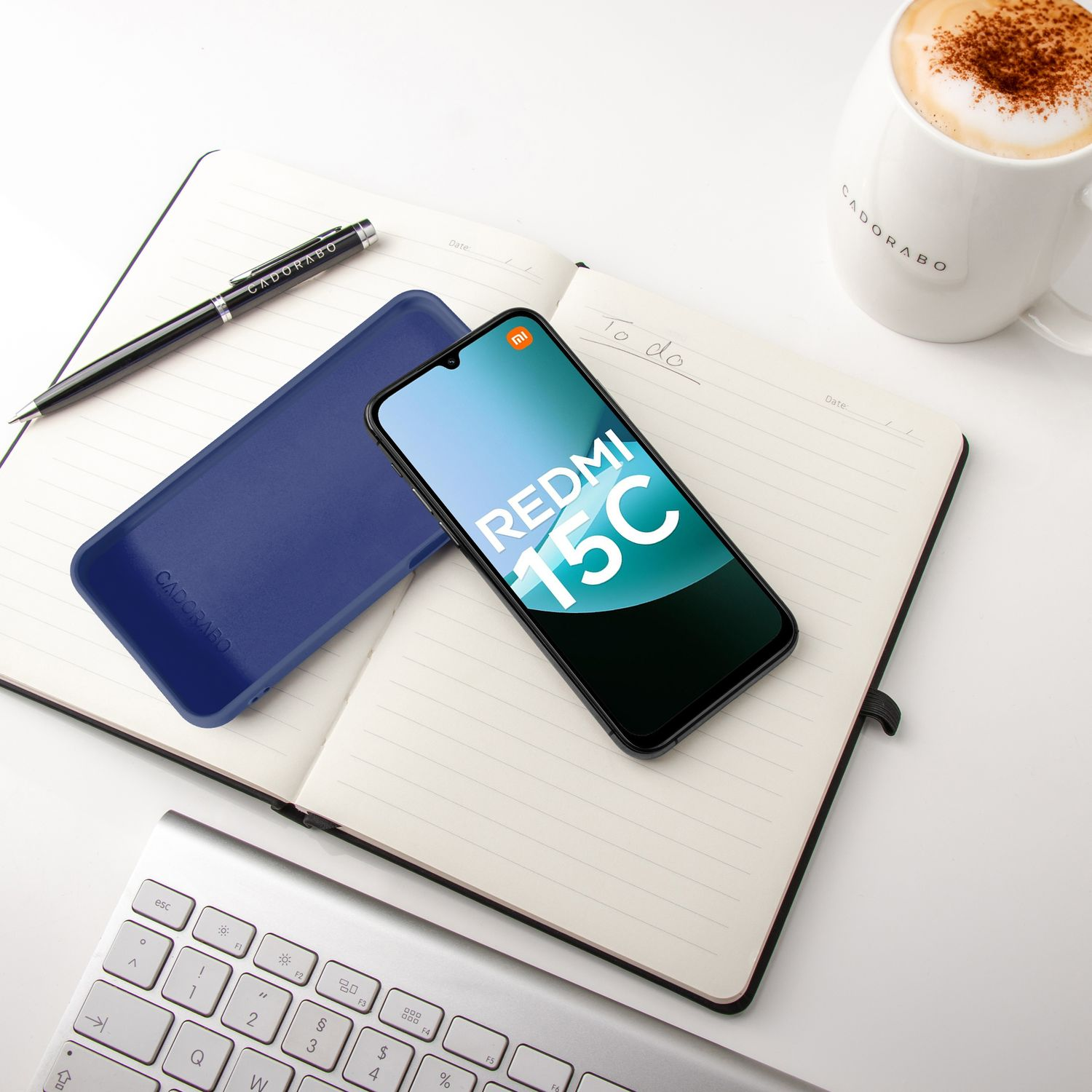 Ein Smartphone liegt auf einem Notizbuch neben einer Tasse Kaffee und einer Tastatur.