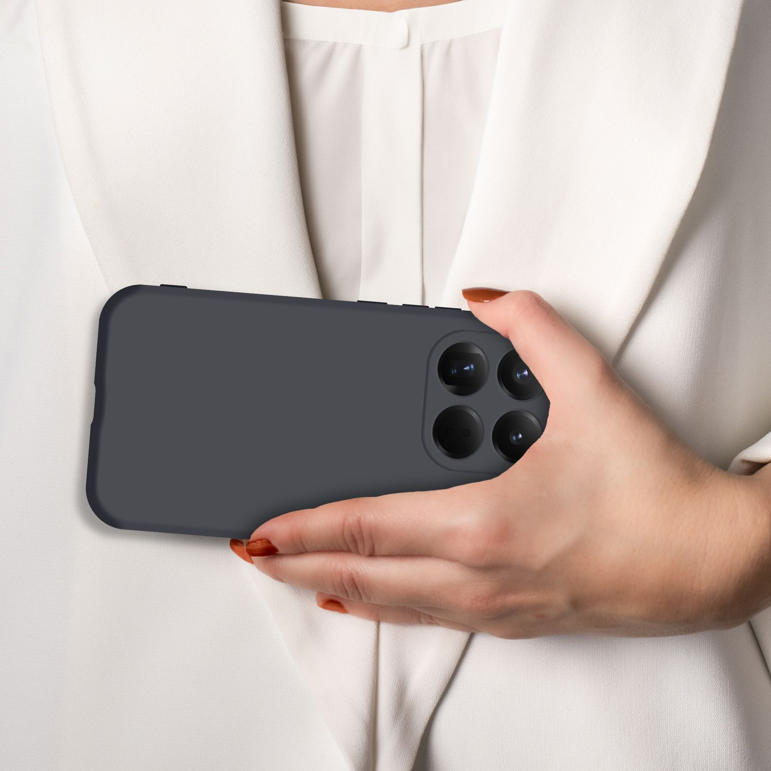 Eine Hand hält ein dunkles Smartphone mit vier Kameras auf einem weißen Hemd.
