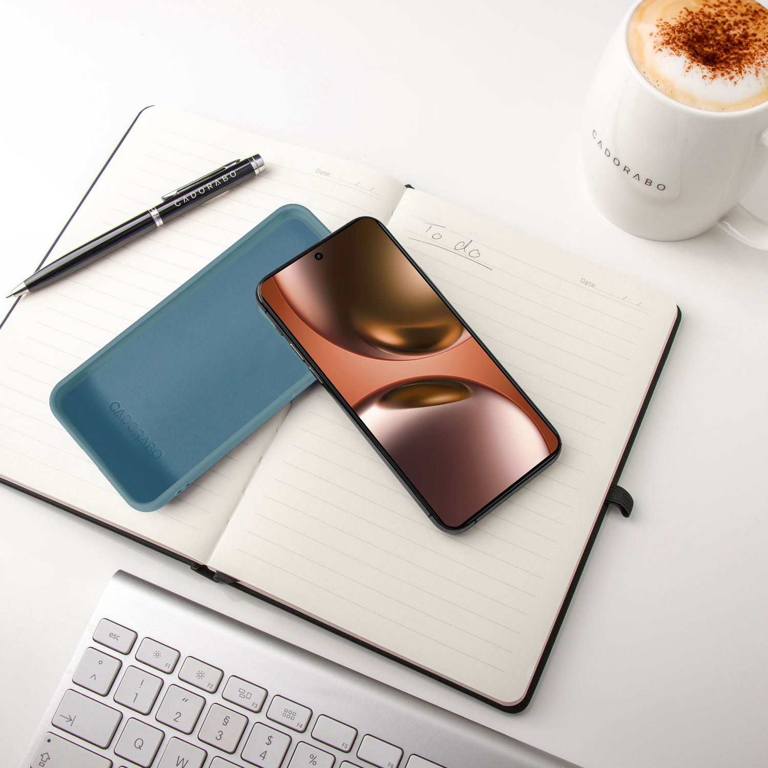 Ein Smartphone, Notizbuch, Stift, Tasse Kaffee und Tastatur auf einem weißen Tisch.