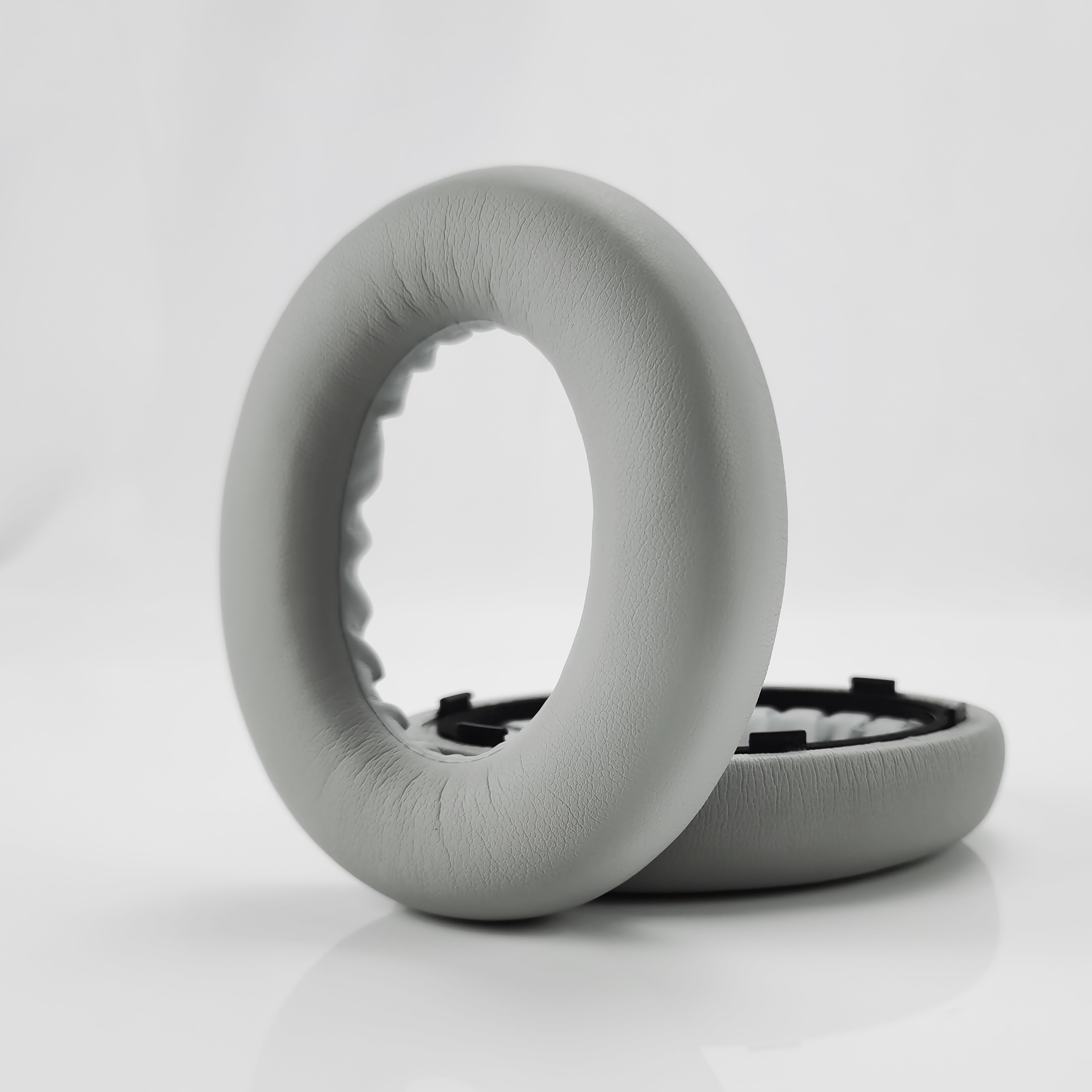 Dwie szare poduszki nauszne do słuchawek leżą obok siebie na białej powierzchni.