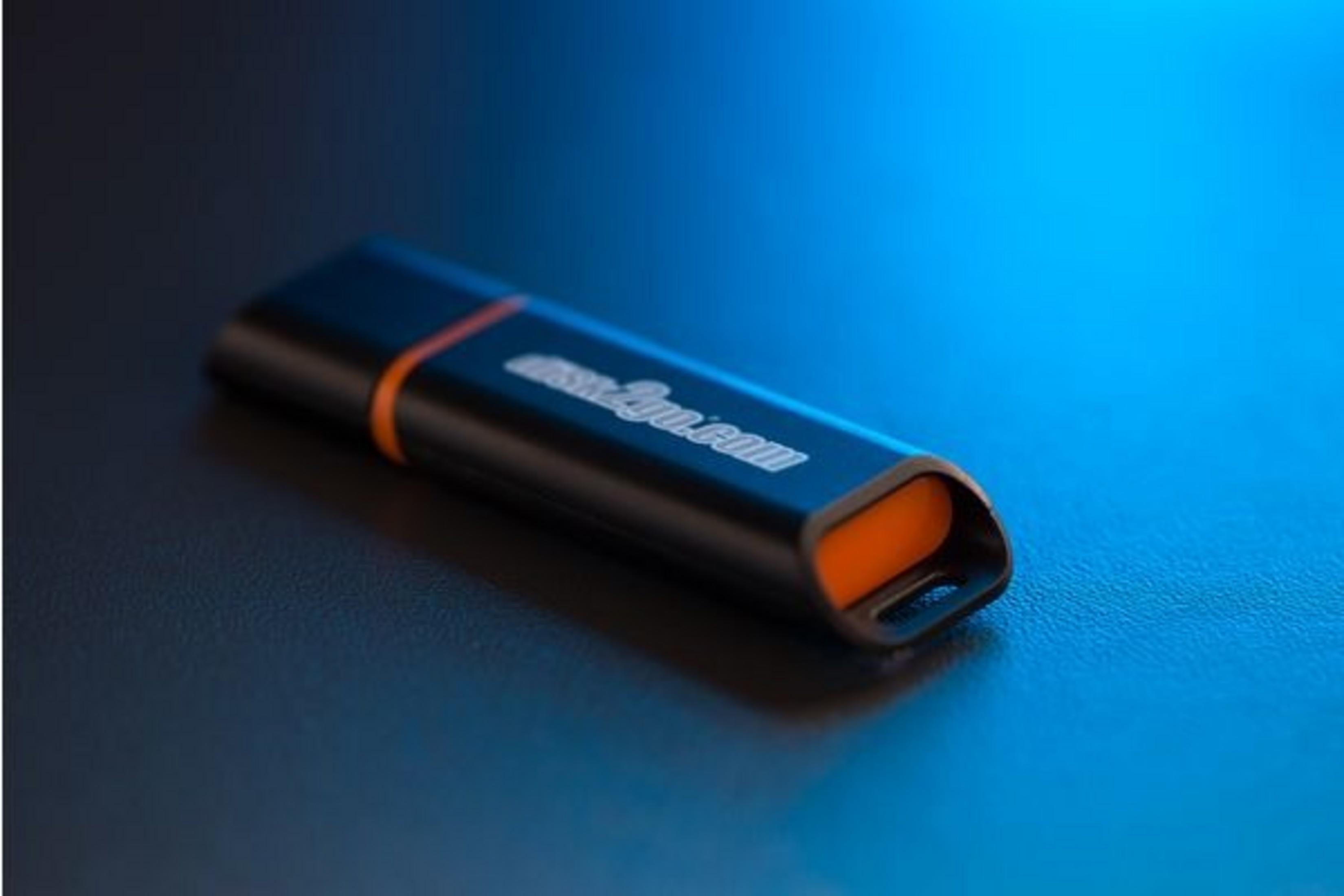 Une clé USB noire avec des accents orange et un logo repose sur une surface sombre.