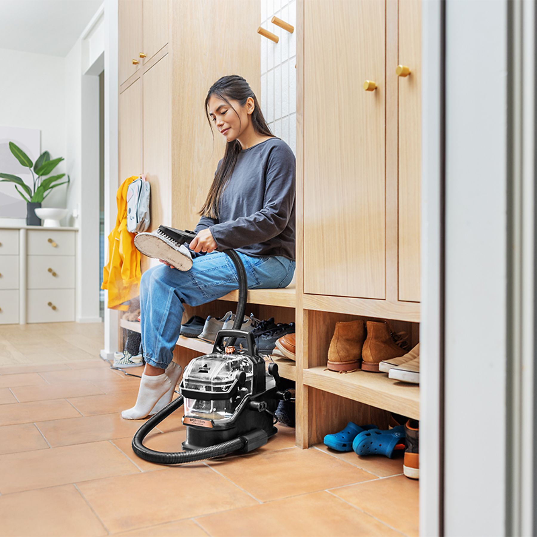 A woman sits on a bench cleaning shoes with a portable cleaning device.