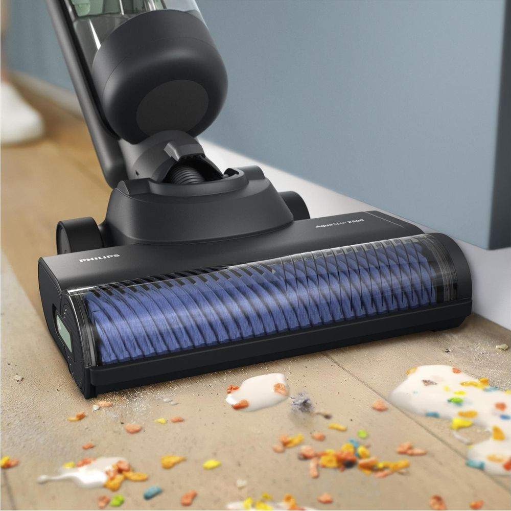 Czarny odkurzacz bezprzewodowy czyści rozlane płatki i mleko z drewnianej podłogi.