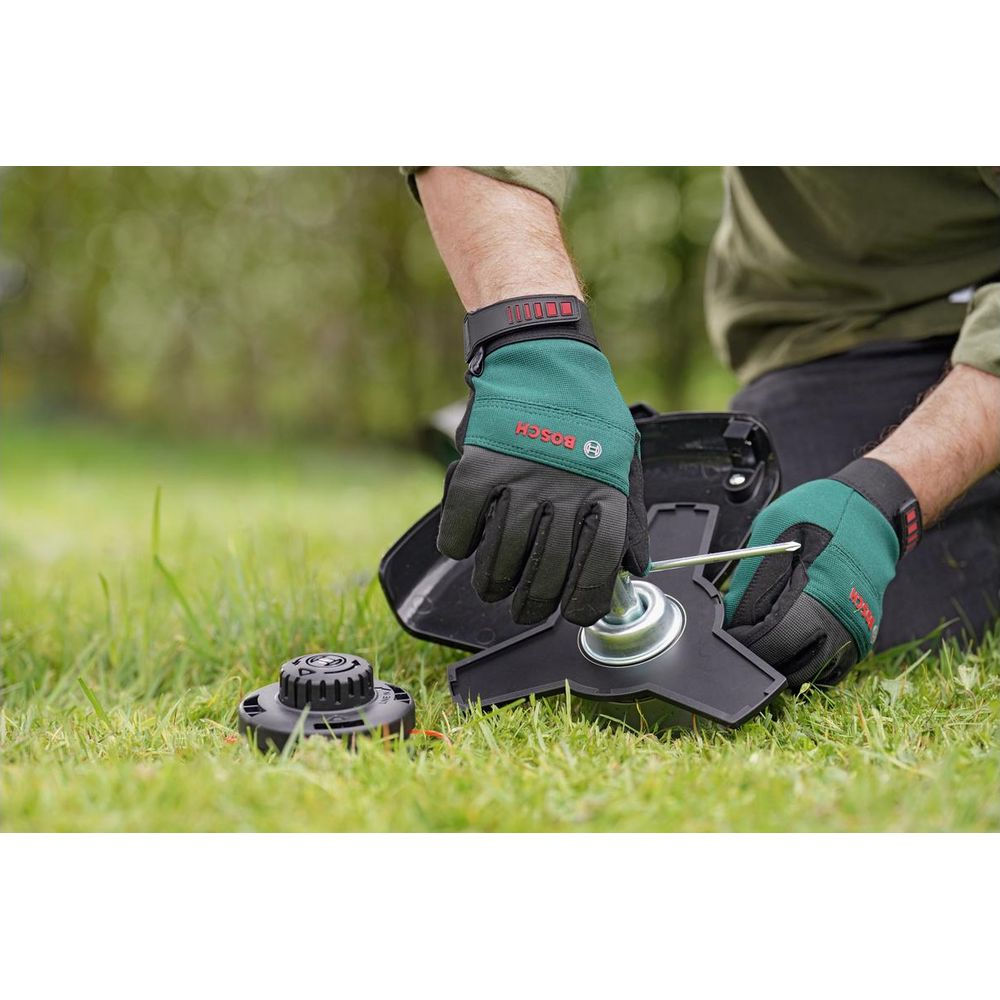 Mann mit grünen Handschuhen repariert Rasentrimmer auf Gras.