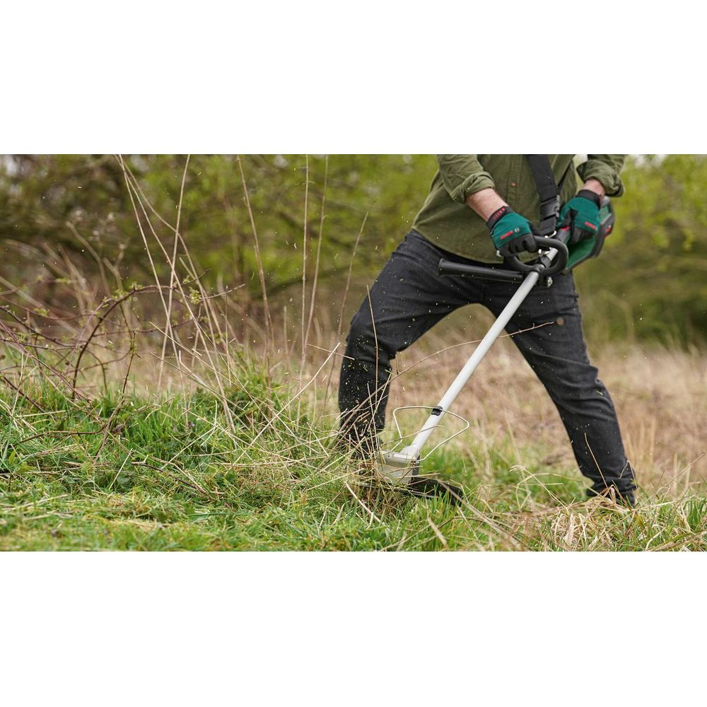 Mann mit Motorsense im Gras, grüne Handschuhe, schwarze Hose.
