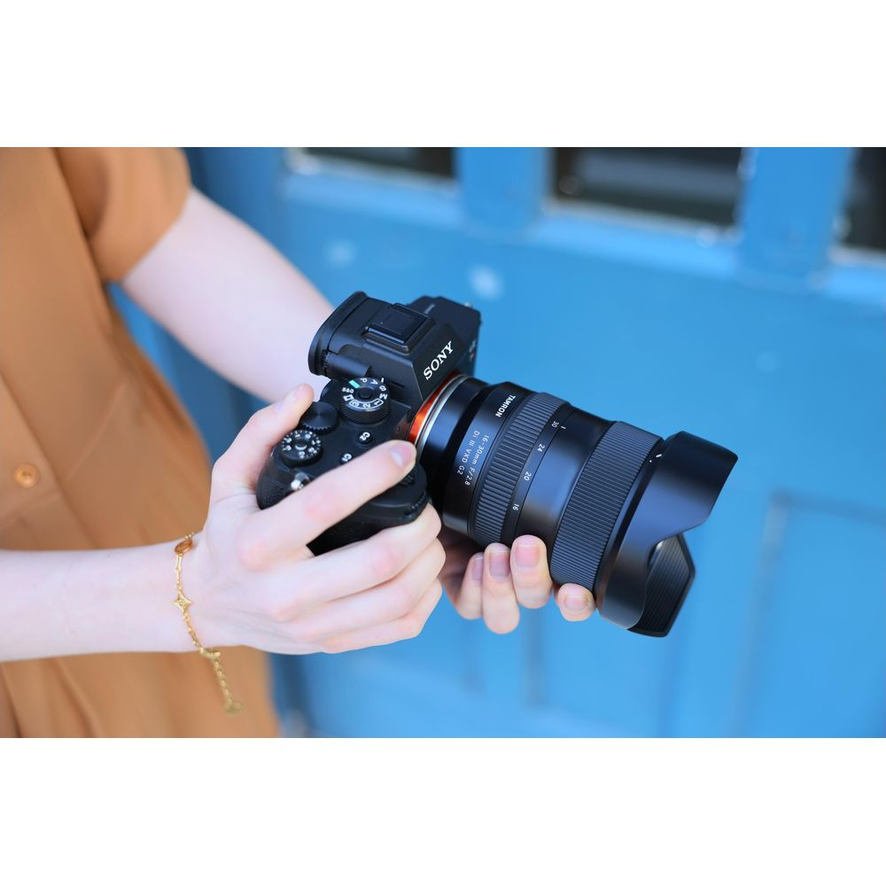 Een persoon in bruine jurk houdt een Sony camera met Tamron lens vast.