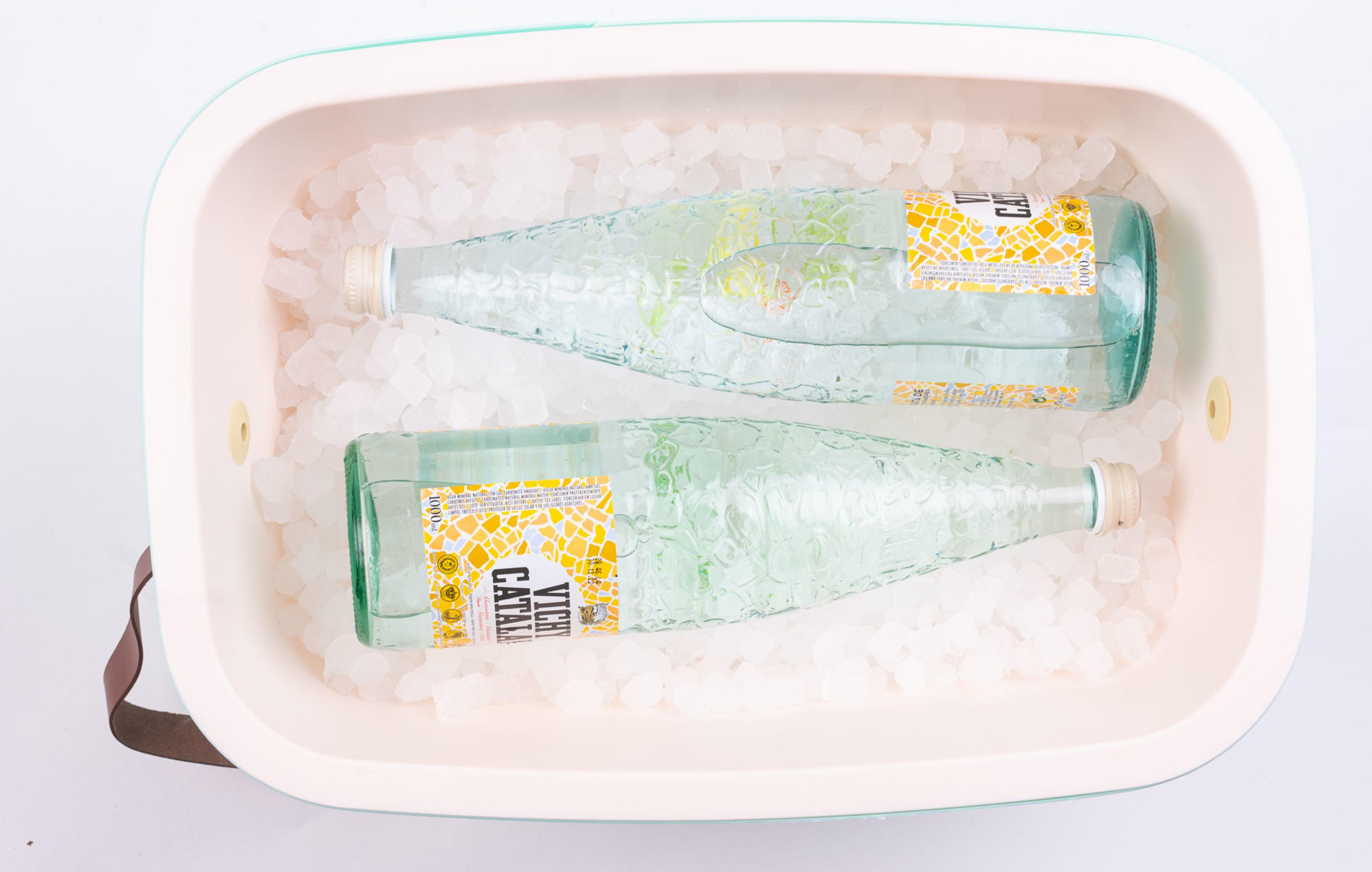 Dos botellas de vidrio de Vichy Catalan en cubitos de hielo dentro de un recipiente.