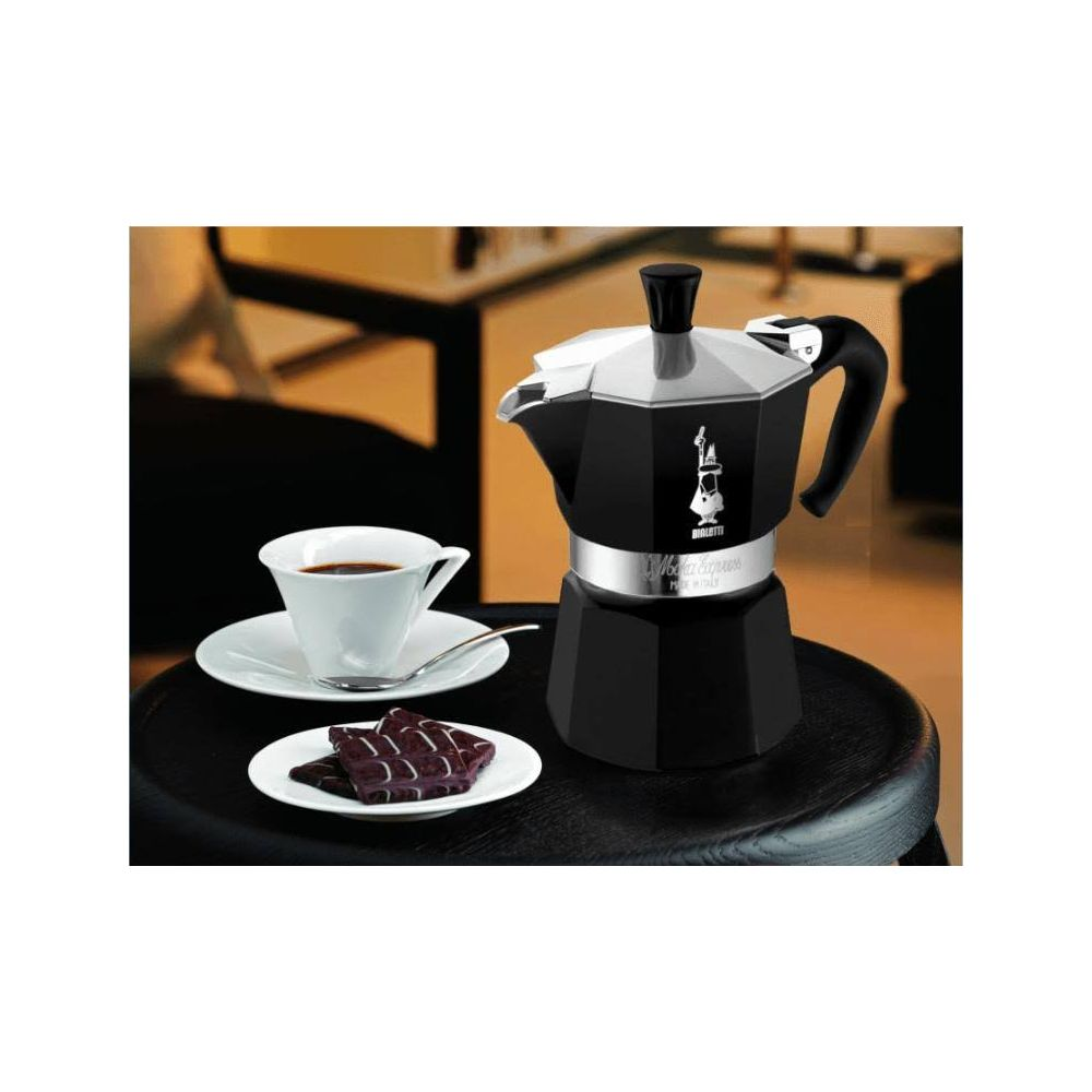 Czarna kawiarka z filiżanką kawy i czekoladą na drewnianym stole.