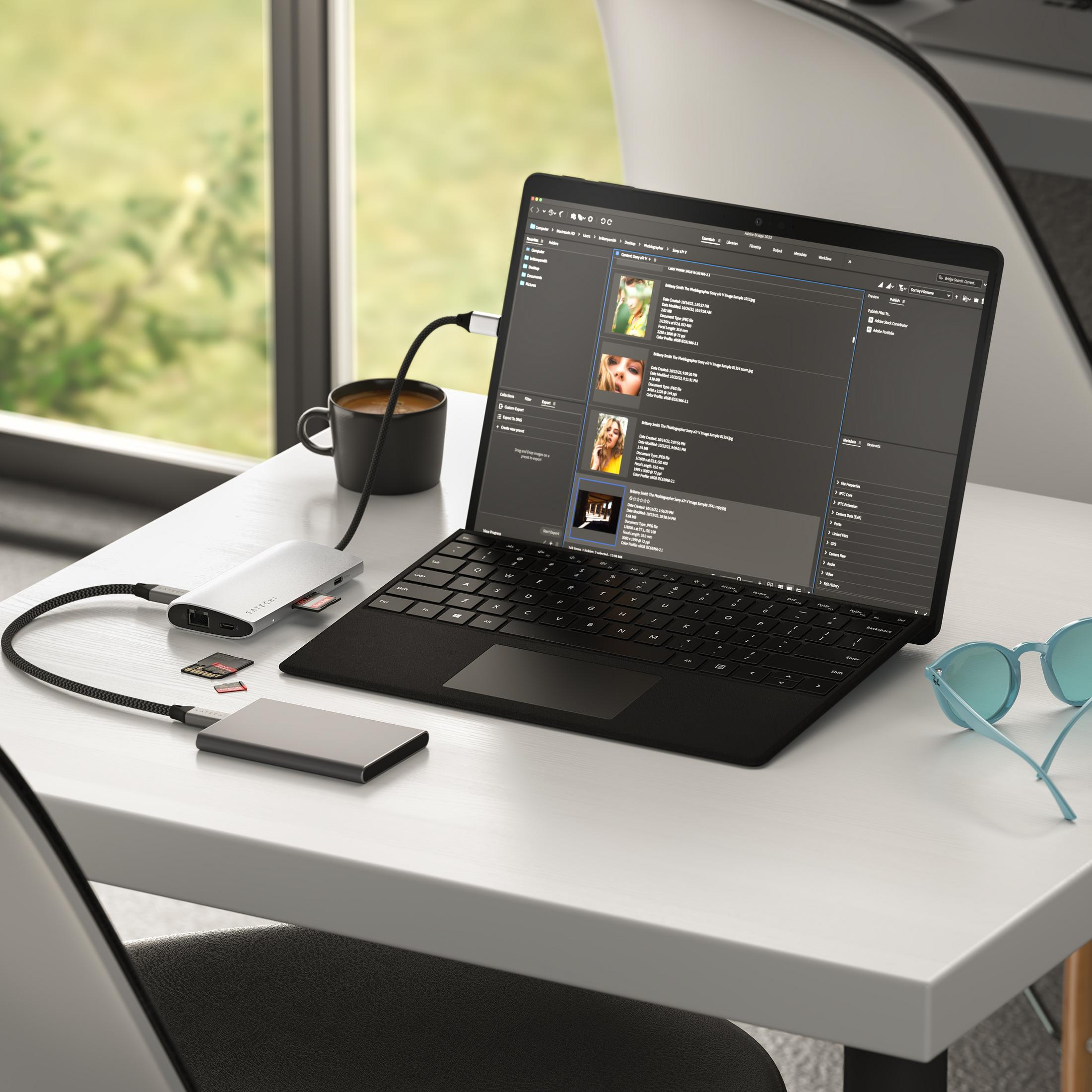 Laptop con hub Satechi, schede SD e caffè su una scrivania.