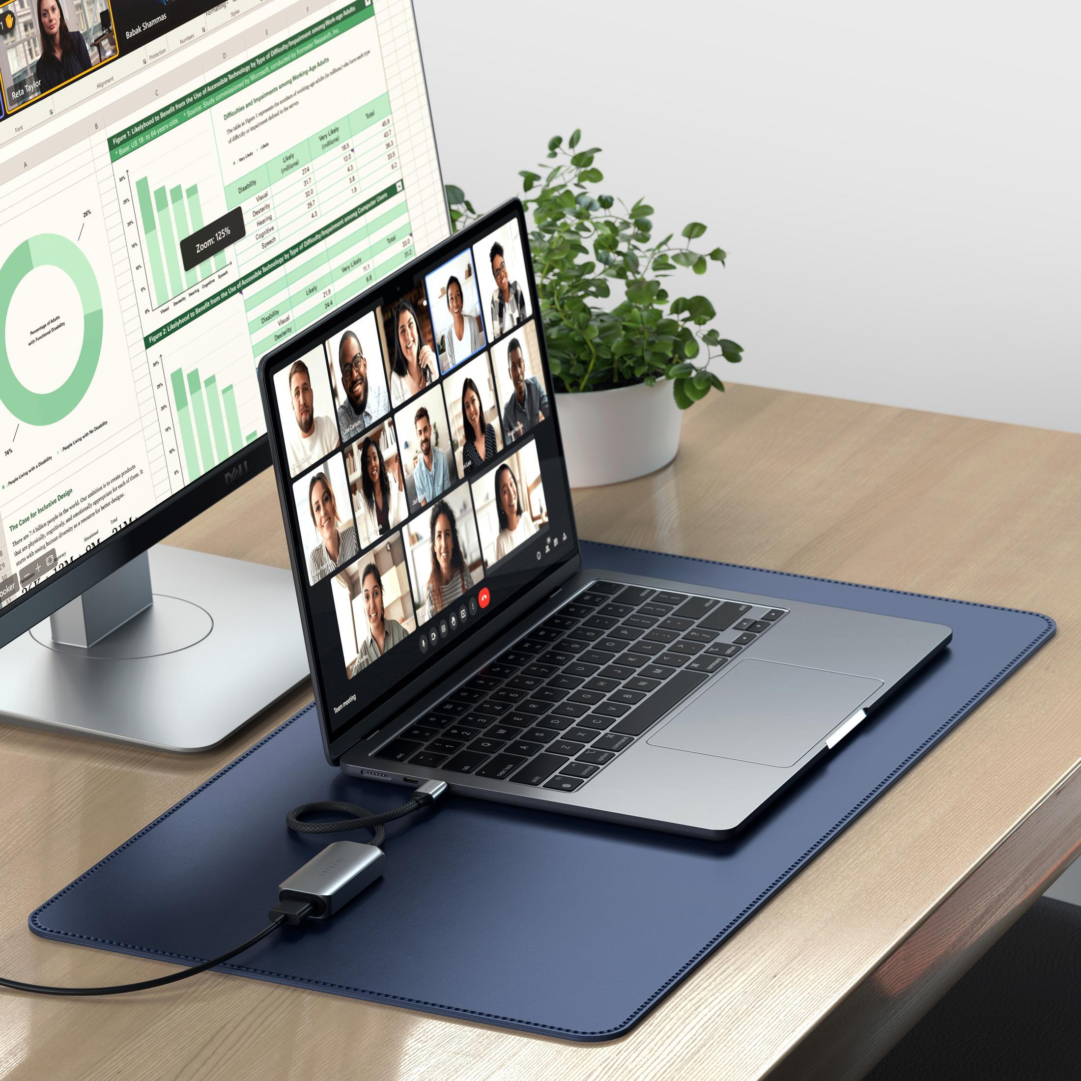 Un laptop mostra una riunione online con molti volti. Un monitor esterno accanto mostra grafici.