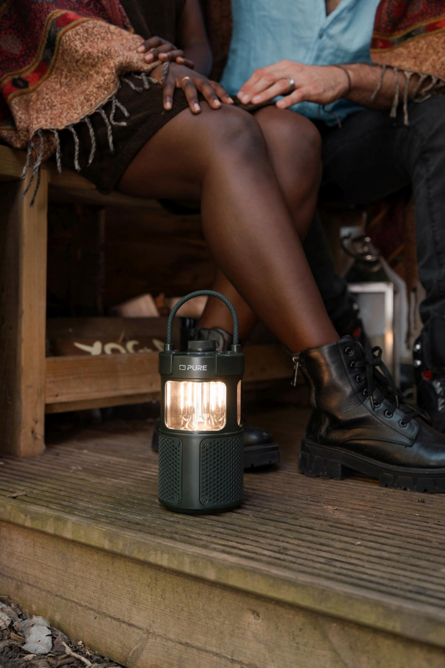 Para siedzi na drewnianym tarasie z latarnią i głośnikiem.