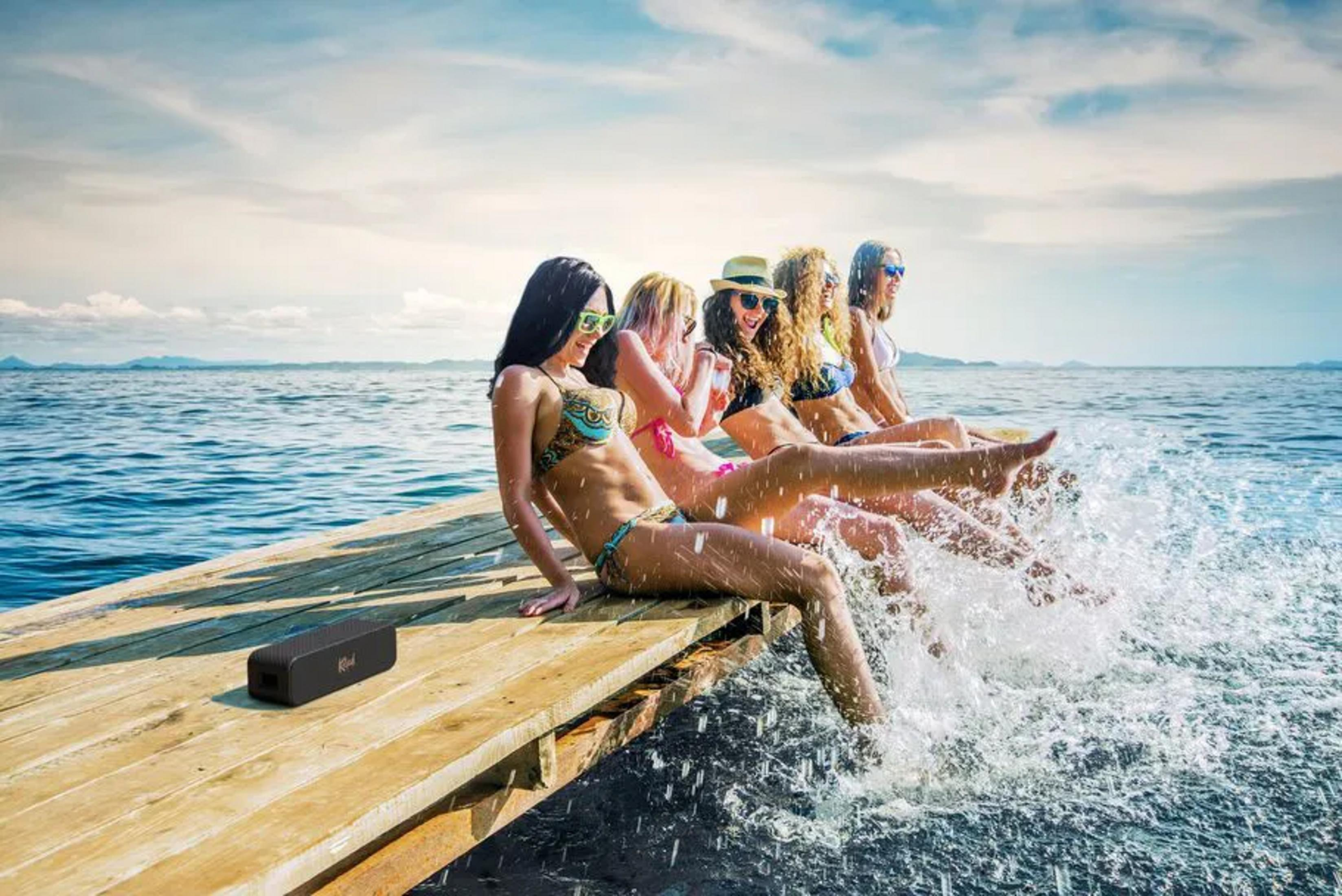 Pięć kobiet na pomoście z głośnikiem, pluskająca woda.