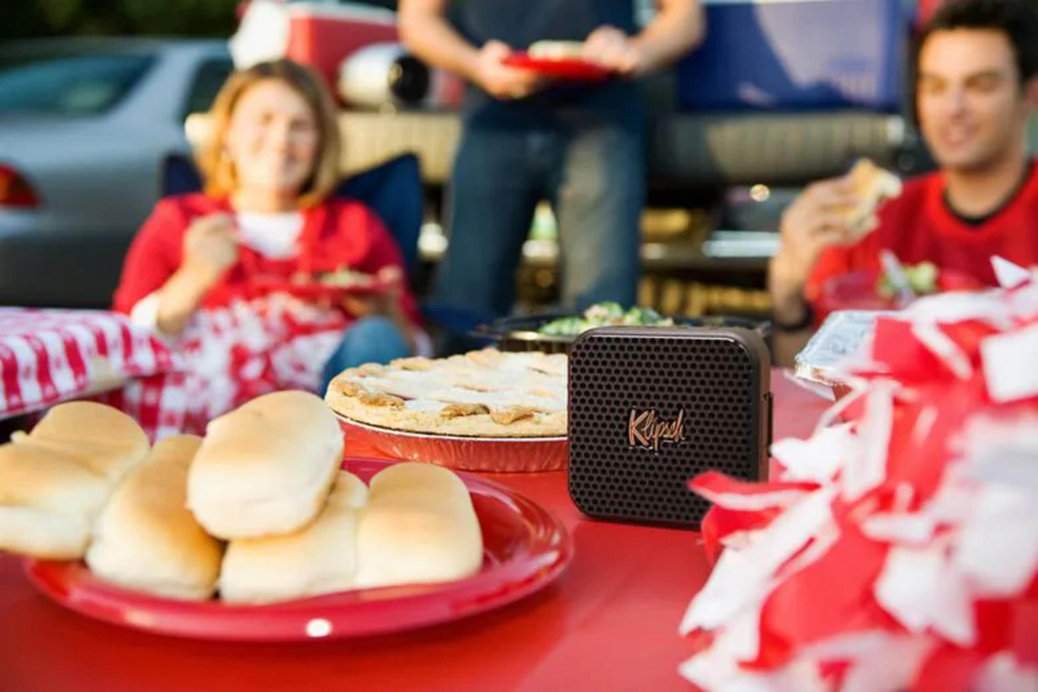 Ludzie cieszą się jedzeniem i muzyką na pikniku z przenośnym głośnikiem.