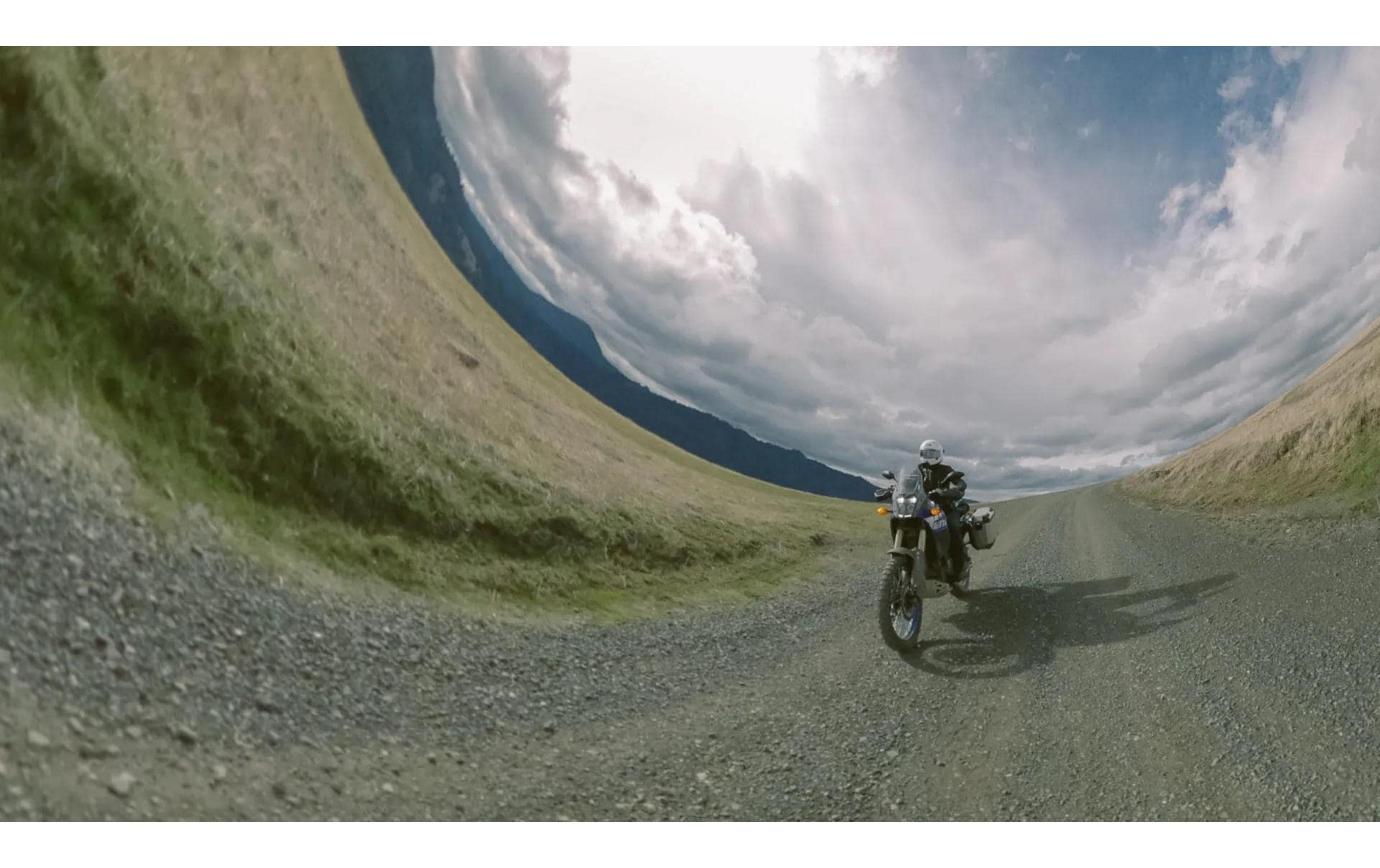 Jazda motocyklem po szutrowej drodze w pagórkowatym krajobrazie pod zachmurzonym niebem.