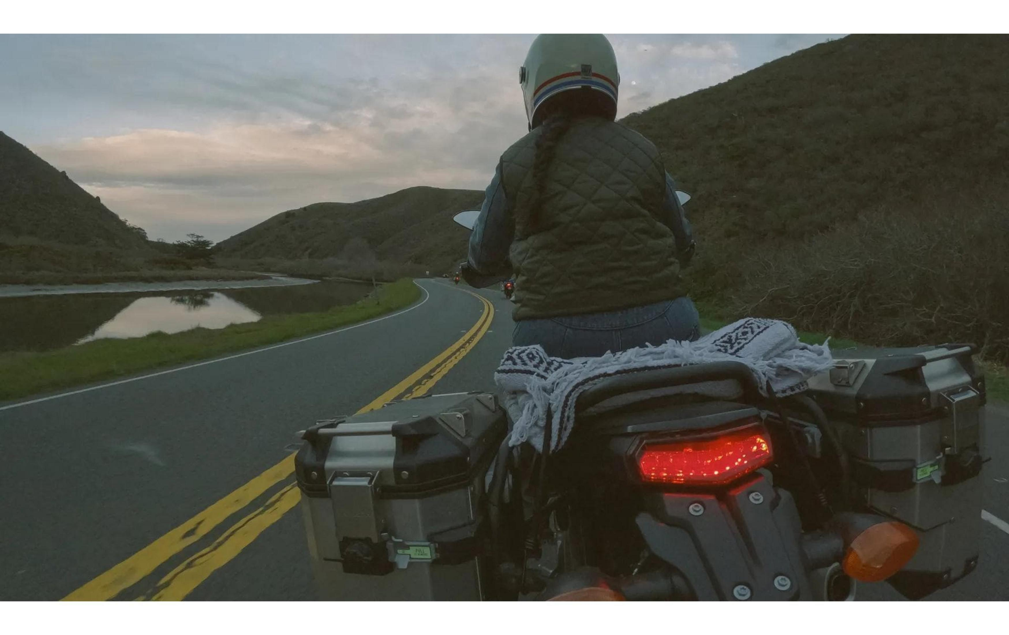Motociclista su una strada con montagne e lago al tramonto.