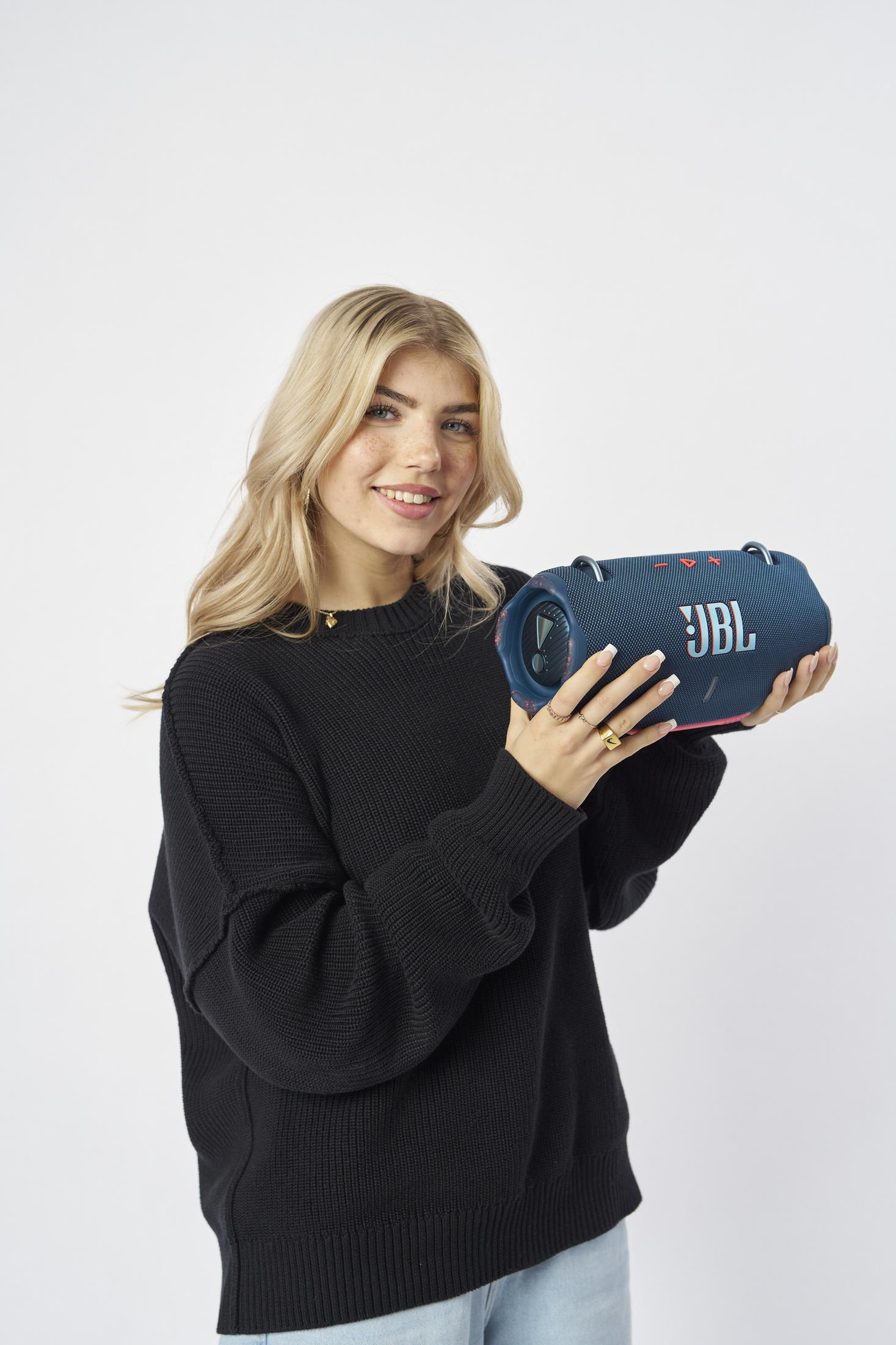 Kobieta z blond włosami trzyma niebieski głośnik JBL w studiu.