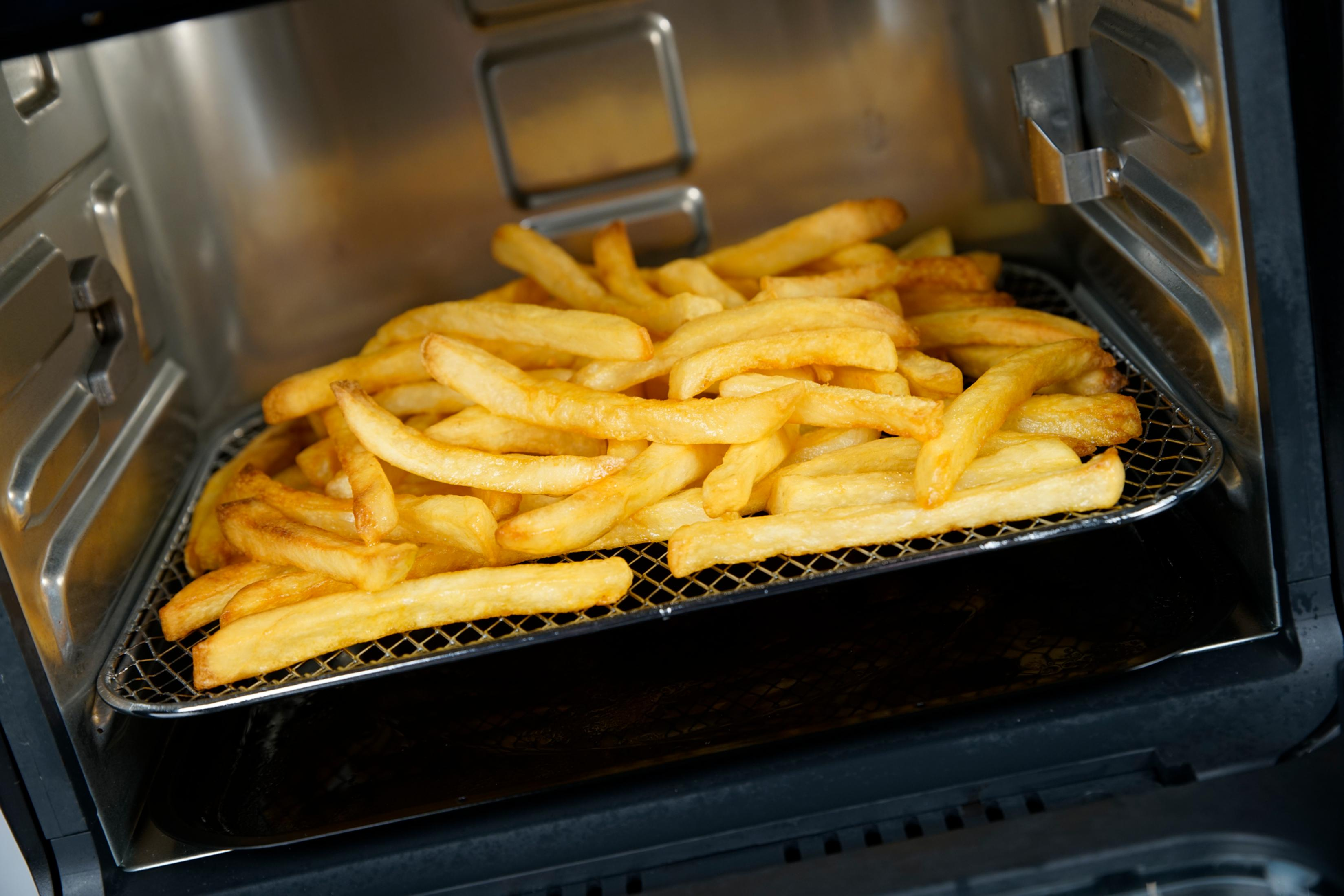 Goldbraune Pommes Frites auf einem Rost in einem Airfryer.