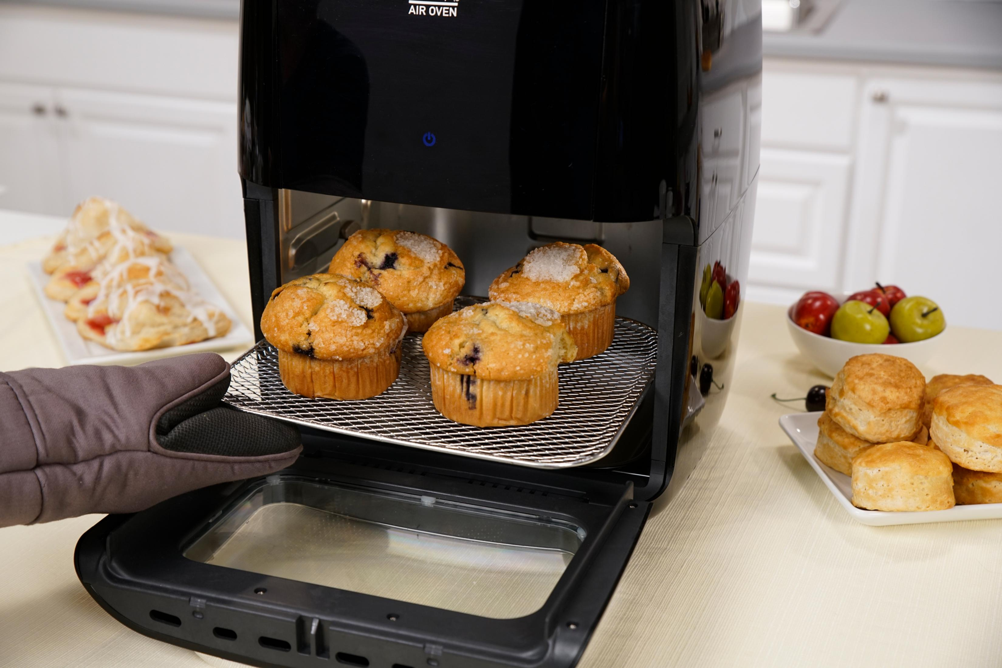 Ein Handschuh zieht ein Blech mit Muffins aus einem schwarzen Heißluftofen.