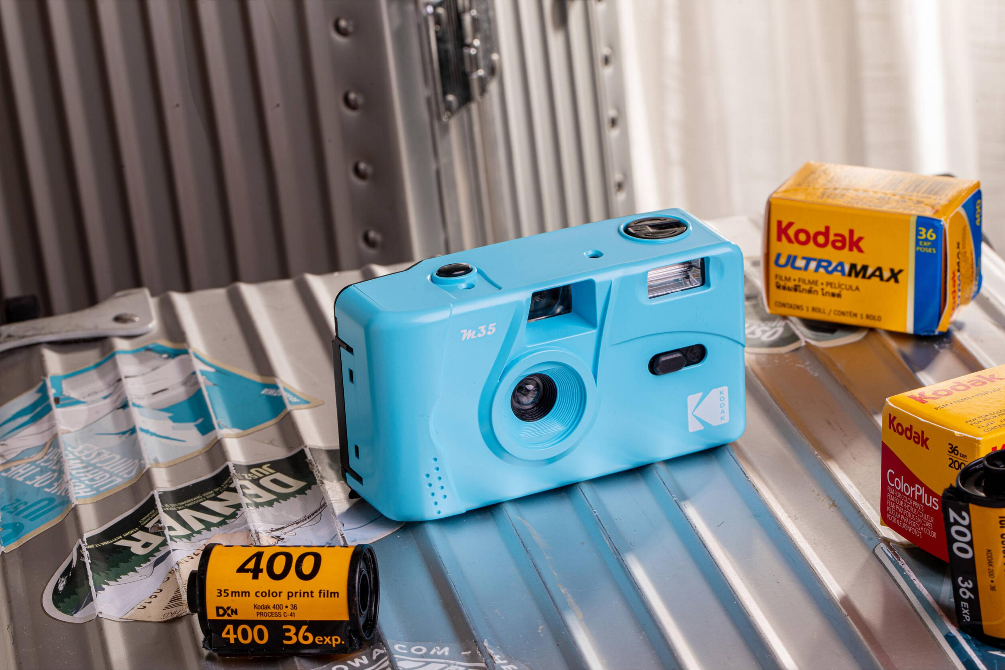 Una cámara Kodak azul claro con película y empaques Kodak sobre una superficie acanalada.