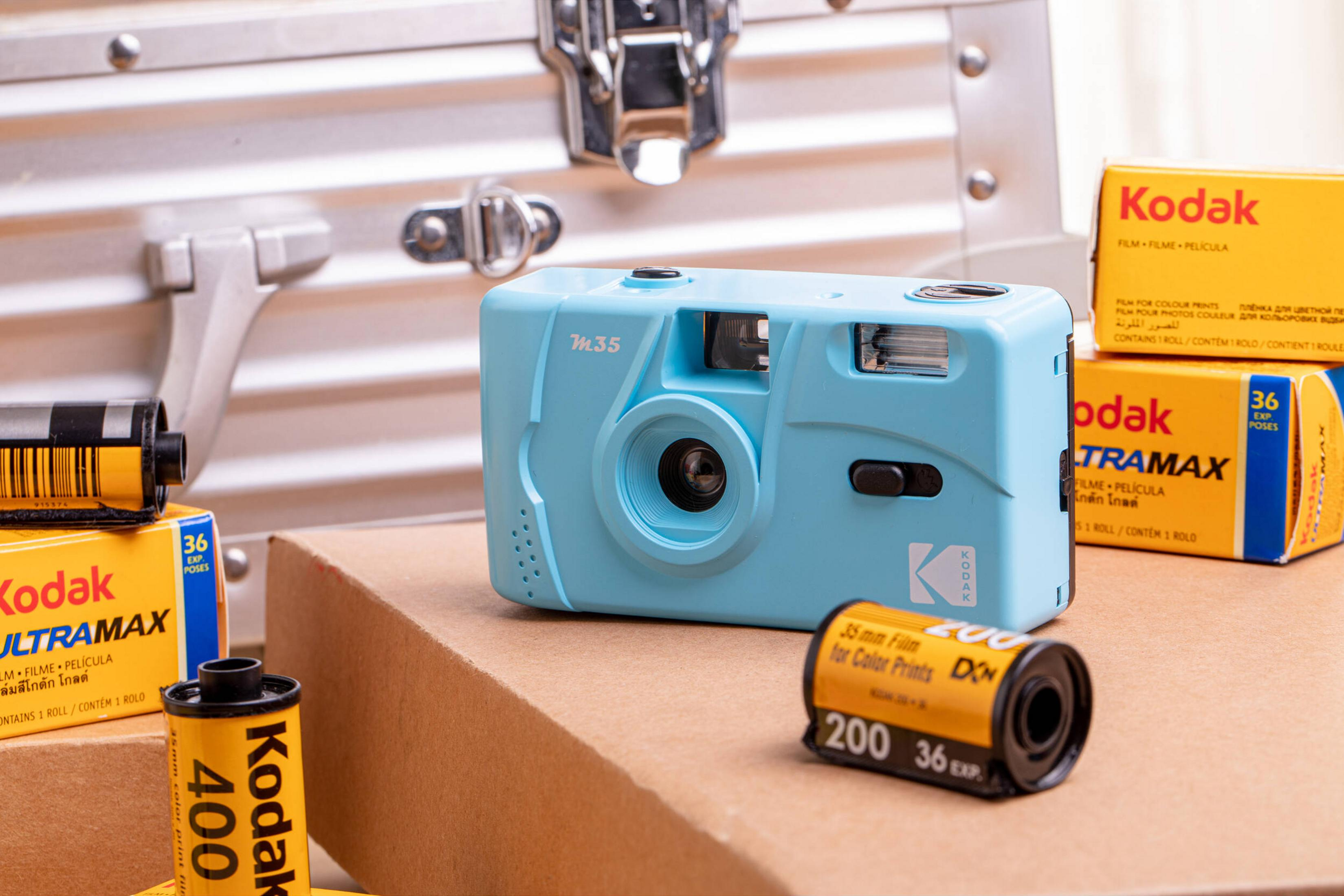 Una cámara de película azul claro se sienta con cajas y rollos de película Kodak.