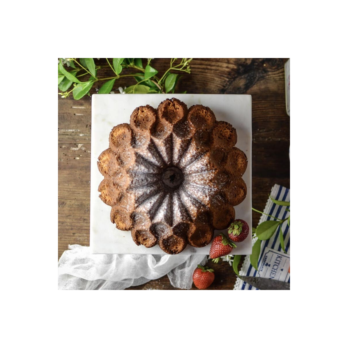 Pudra şekeri serpilmiş ve çileklerle süslenmiş bir bundt kek.