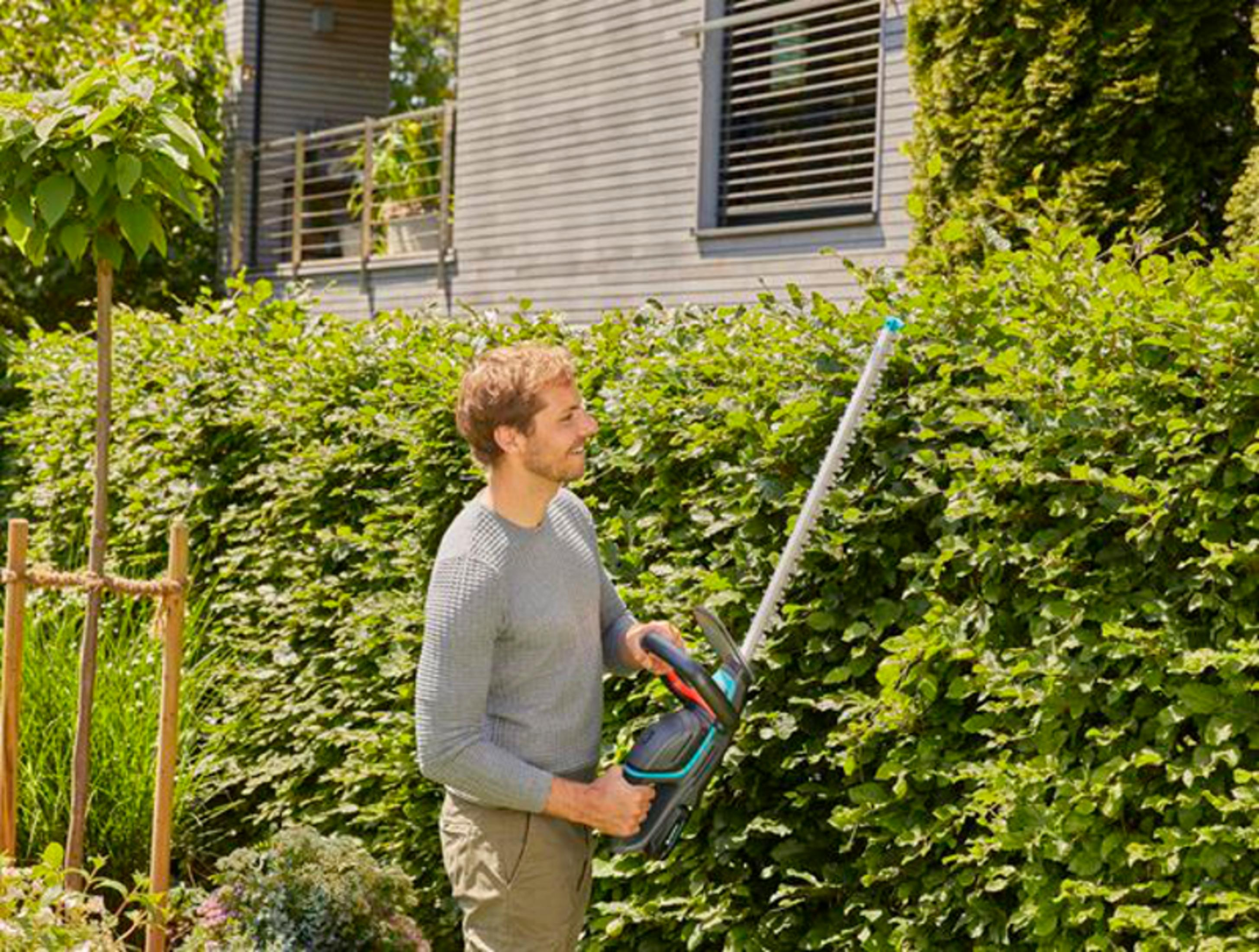 Mężczyzna przycina żywopłot nożycami elektrycznymi przed domem.