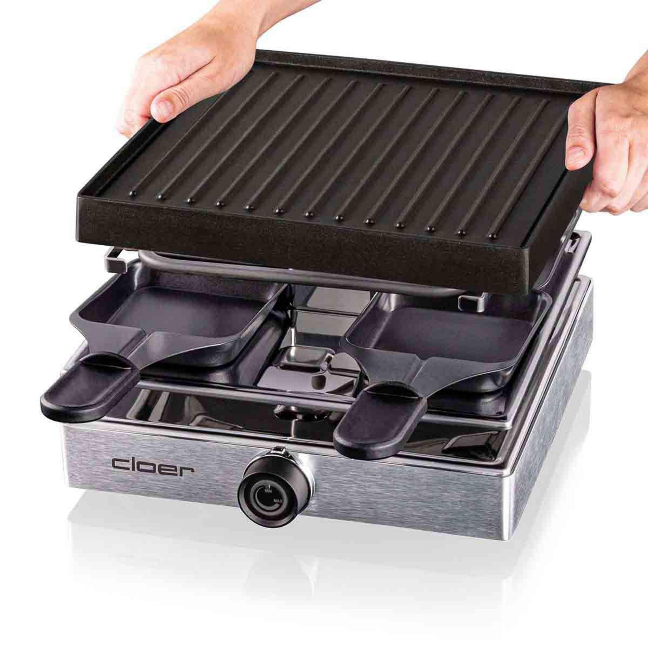 Zwei Hände halten eine Grillplatte über einem Raclette-Gerät.