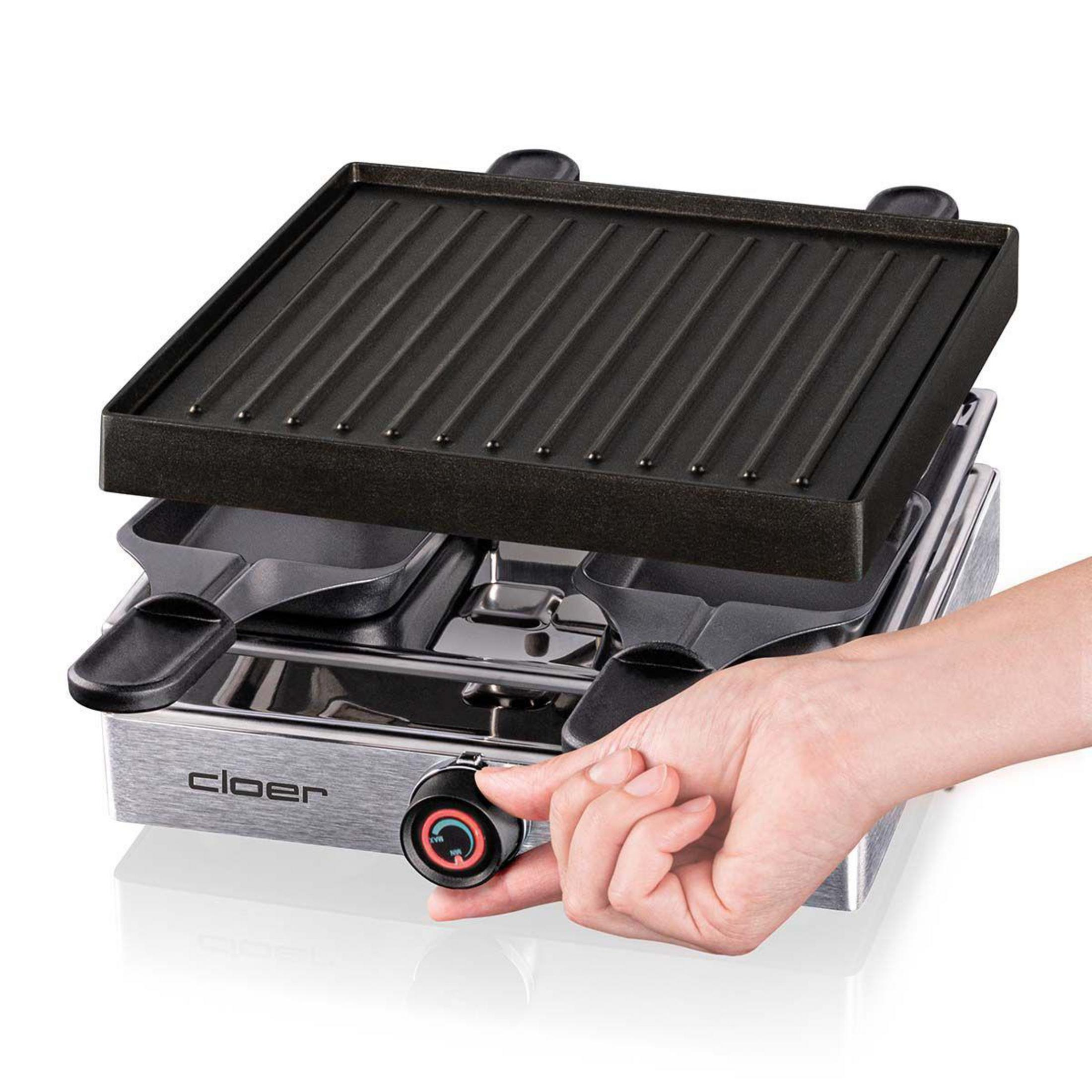 Eine Hand dreht den Temperaturregler eines silbernen Raclette-Grills mit schwarzer Grillplatte.