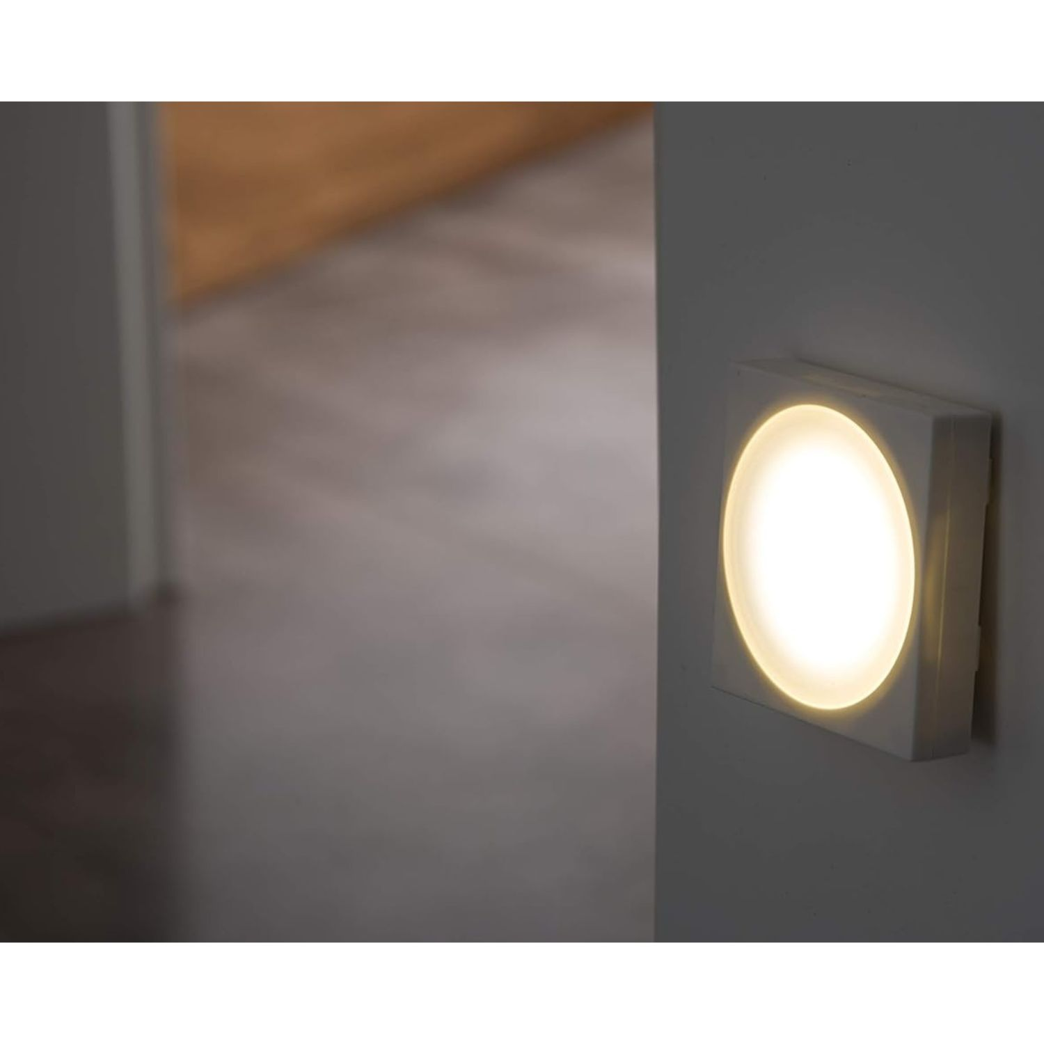 Ein quadratisches Wandlicht mit heller, runder Mitte leuchtet auf einer Wand.