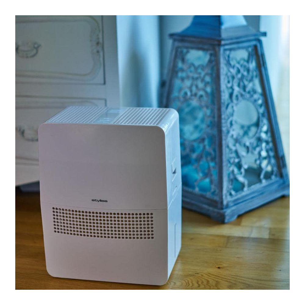 Un purificatore d'aria bianco si trova su un pavimento in legno accanto a una lanterna decorativa.