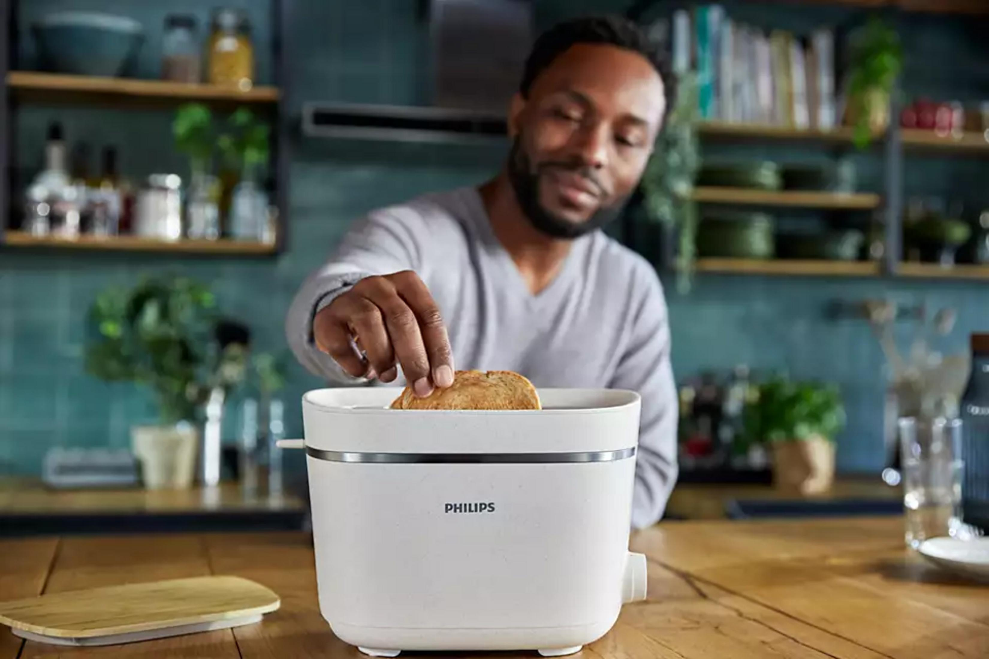 Un uomo mette il pane in un tostapane Philips bianco in cucina.