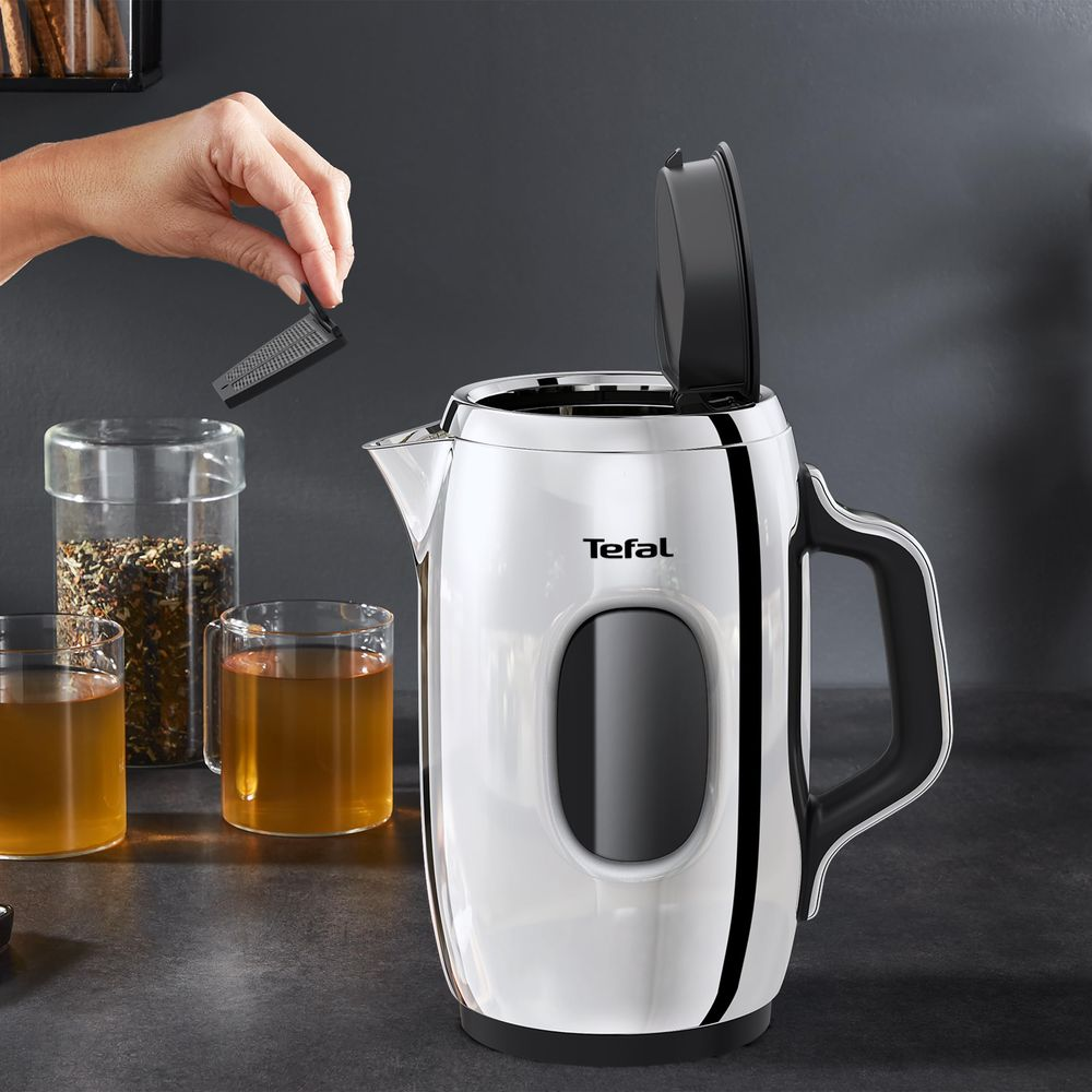 Una mano inserisce un filtro nero in un bollitore bianco Tefal accanto a due bicchieri di tè.